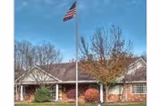 A single-story brick senior living facility with an American flagpole out front and trees.