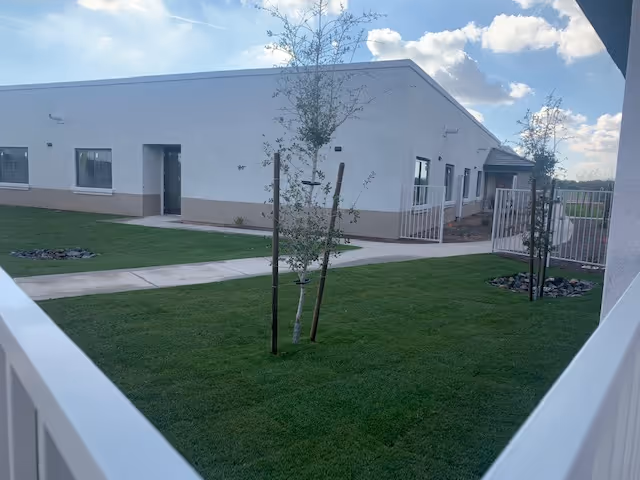 Exterior view of Park Senior Villas - Chandler with white building, green lawn, and trees.