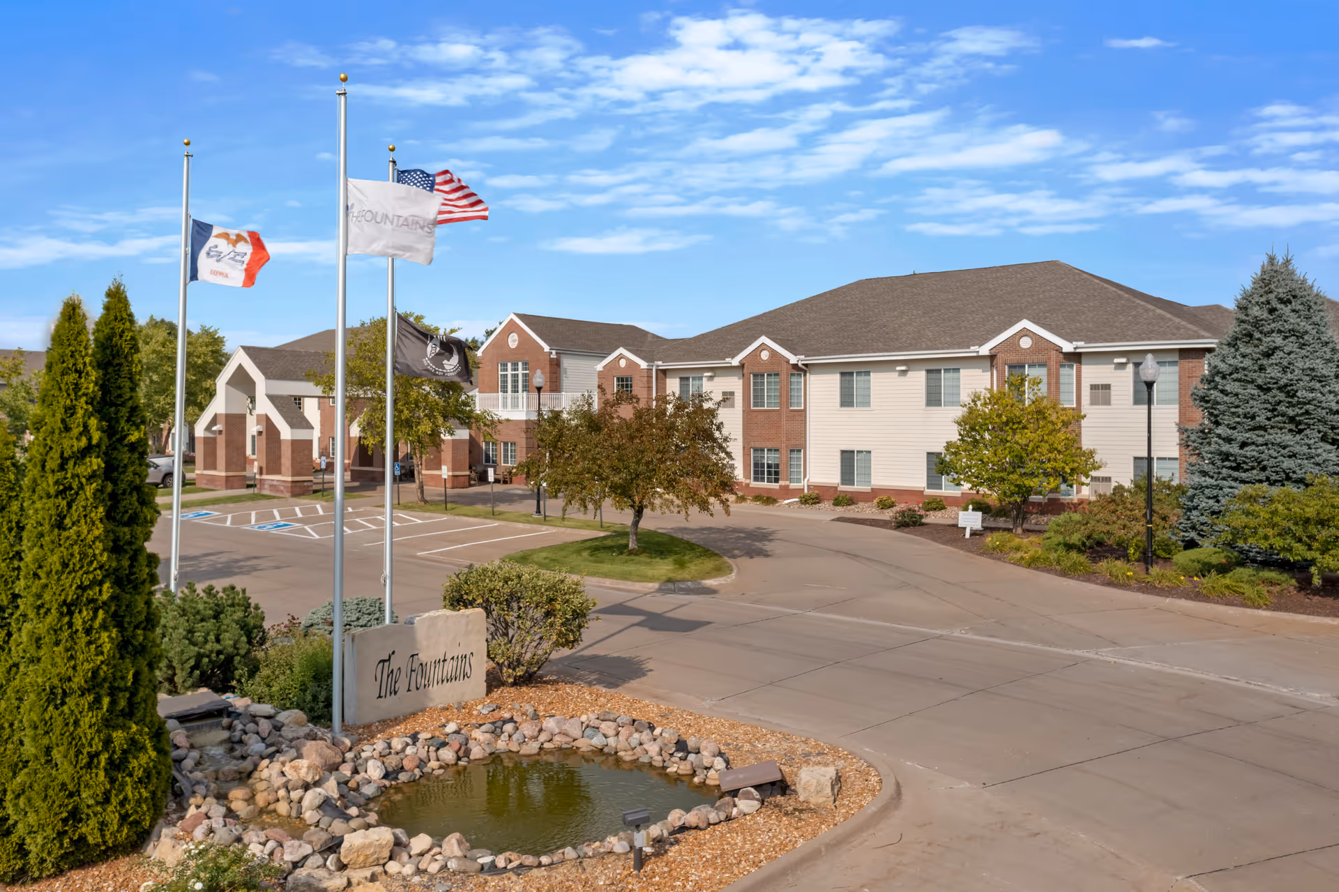 Exterior view of The Fountains senior living campus with flags and landscaped entrance.