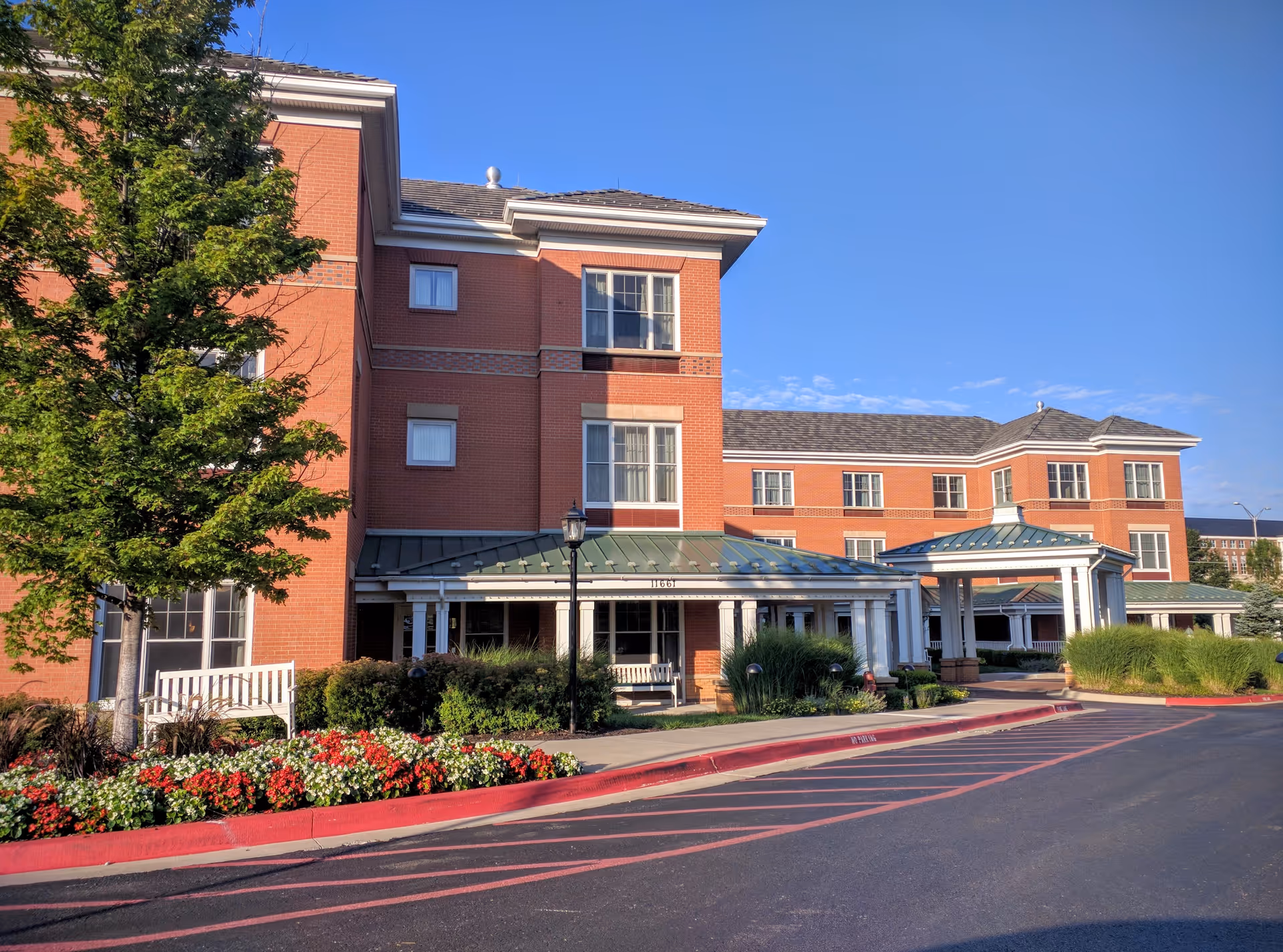 Sunrise of Leawood exterior: brick building with covered entrances, manicured landscaping, under blue sky
