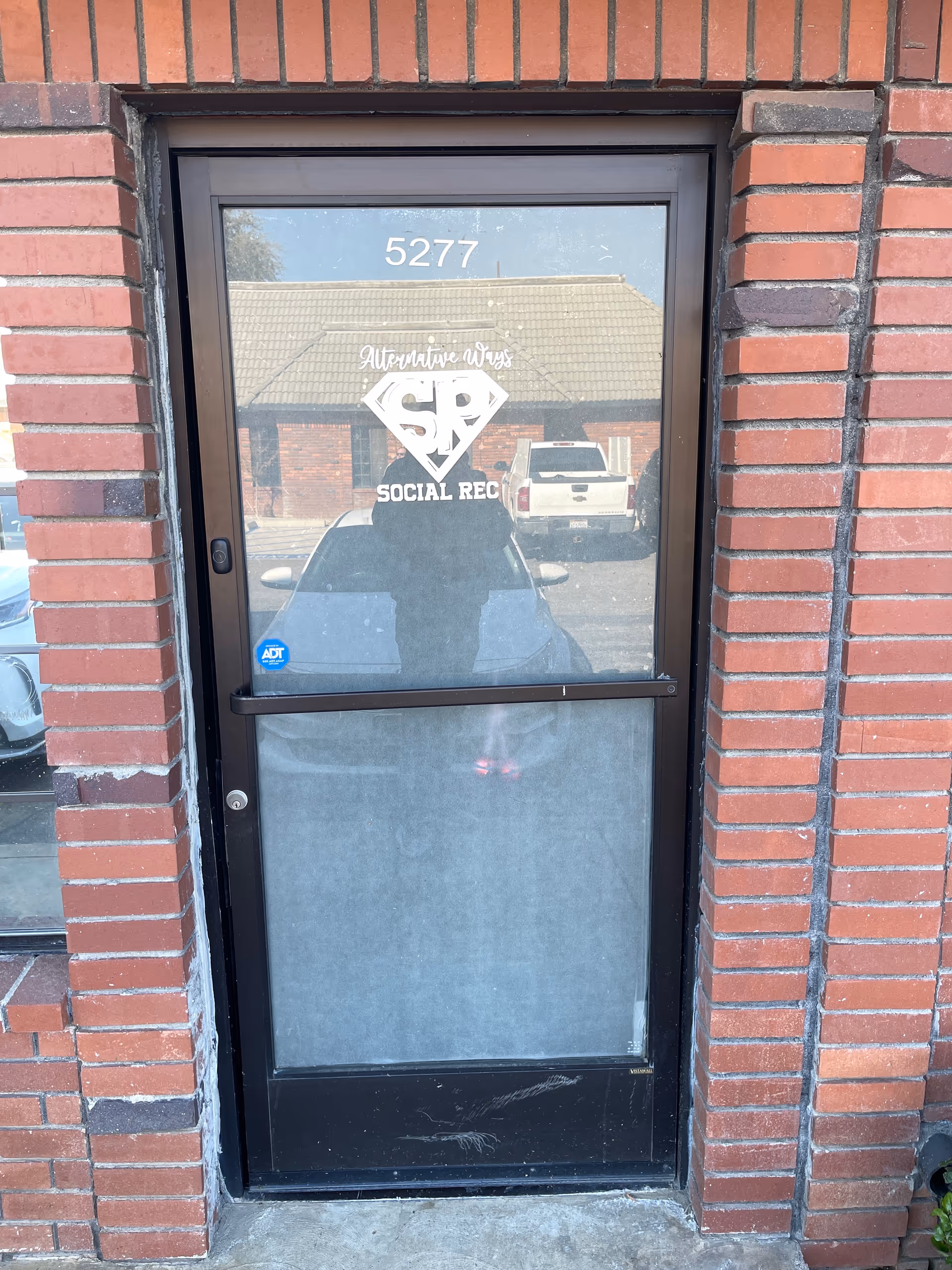 Brick building entrance with a glass door labeled Alternative Ways and a reflected person.