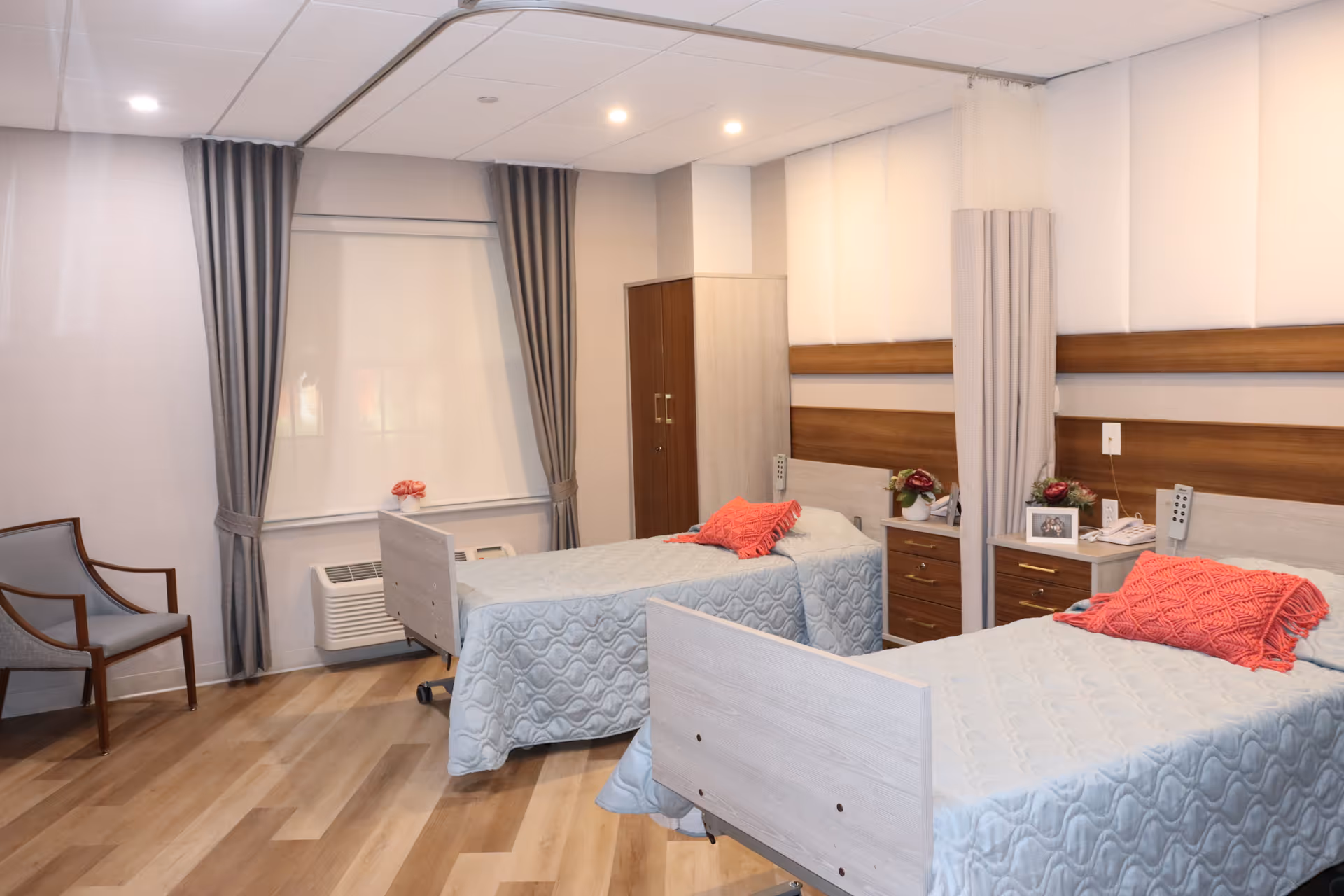 Two single beds in a bright patient room with curtains, nightstands, and decor.