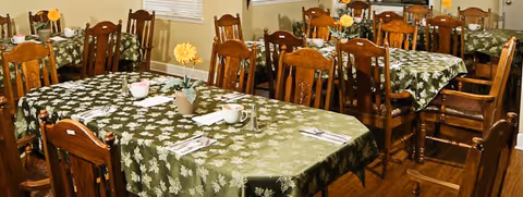 Dining room with multiple wooden tables, green floral tablecloths, and matching chairs.