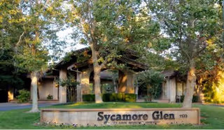 Exterior view of Sycamore Glen Active Senior Community entrance with a stone sign and trees.
