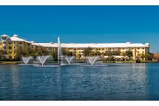 A large, light-colored senior living building across a lake with fountains.