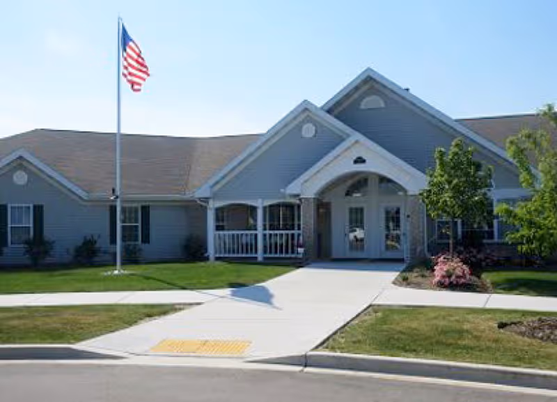Exterior view of Dimensions Living Kenosha facility with entrance, flagpole, and landscaped path.