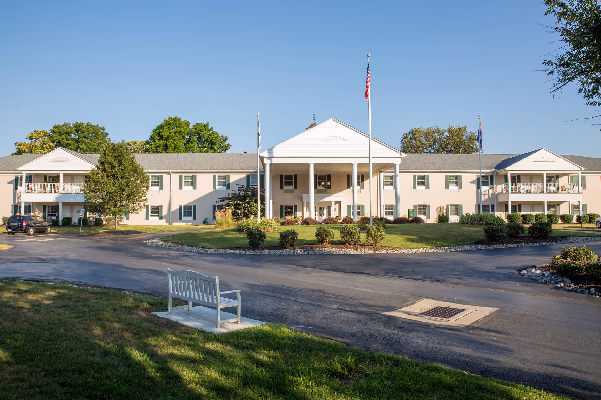 Exterior view of a two-story senior living building with a central entrance and flagpoles.