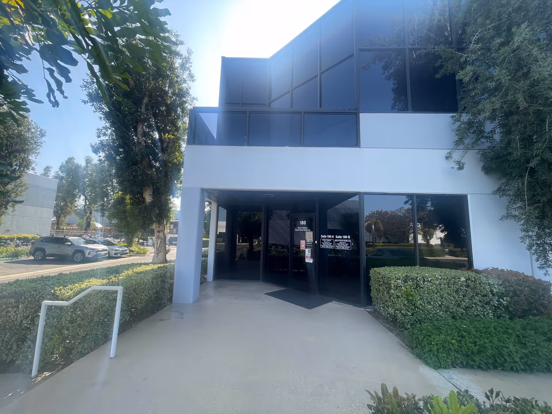 Front entrance of a modern building with glass doors and landscaped hedges.
