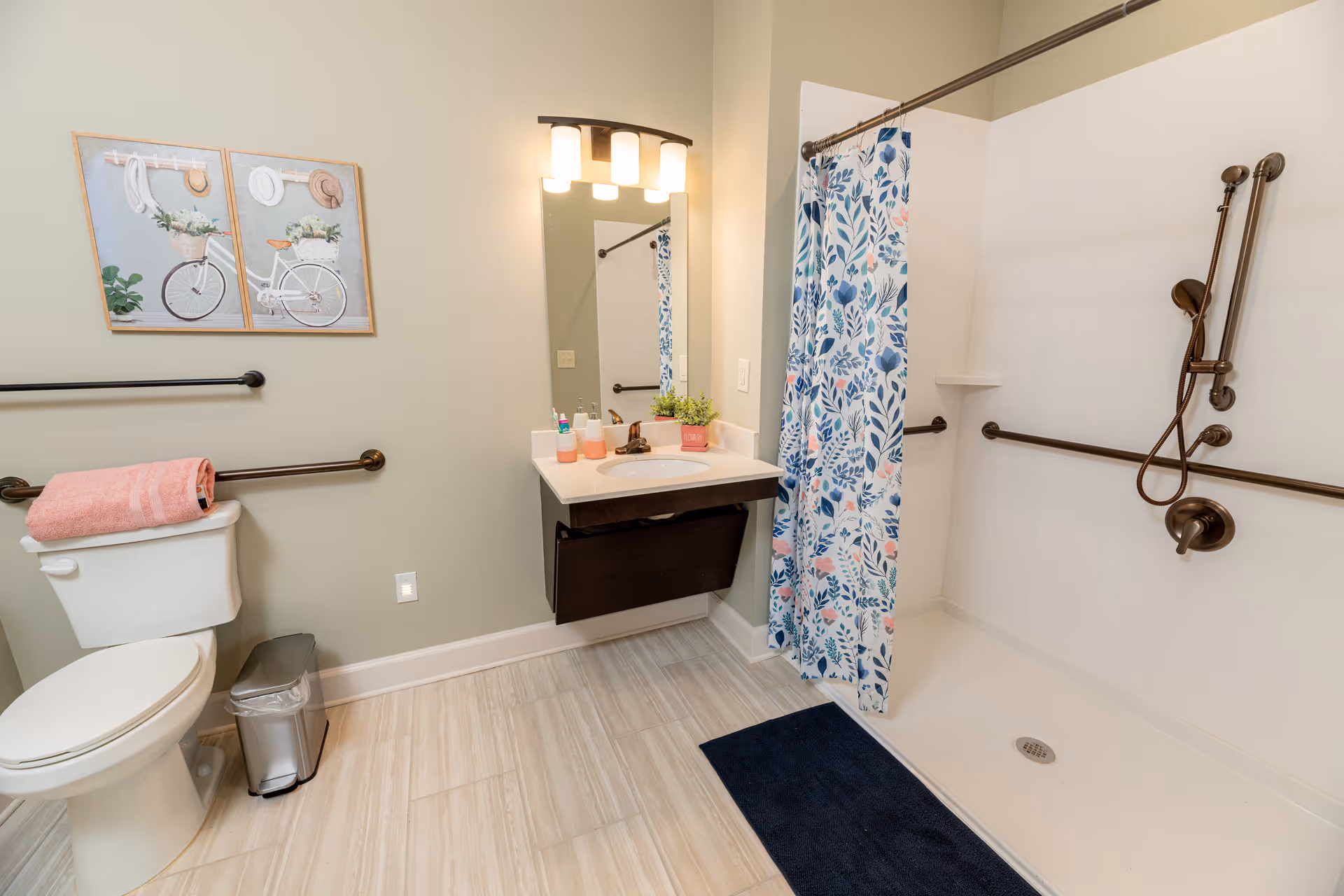 Bathroom with toilet, sink, walk-in shower, blue floral curtain, and grab bars.