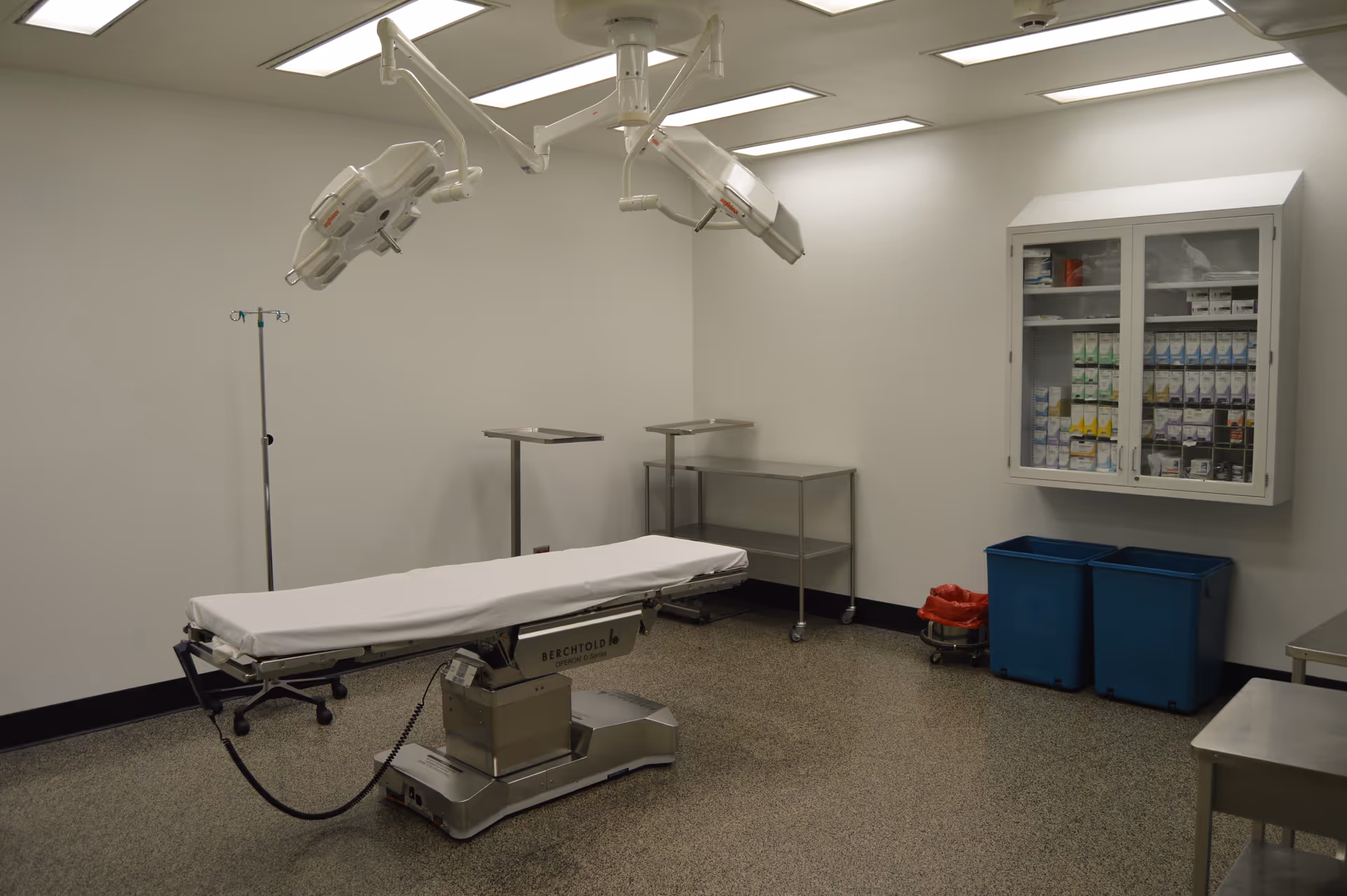 An empty surgical room with ceiling-mounted lights, a surgical table, and medicine cabinets.
