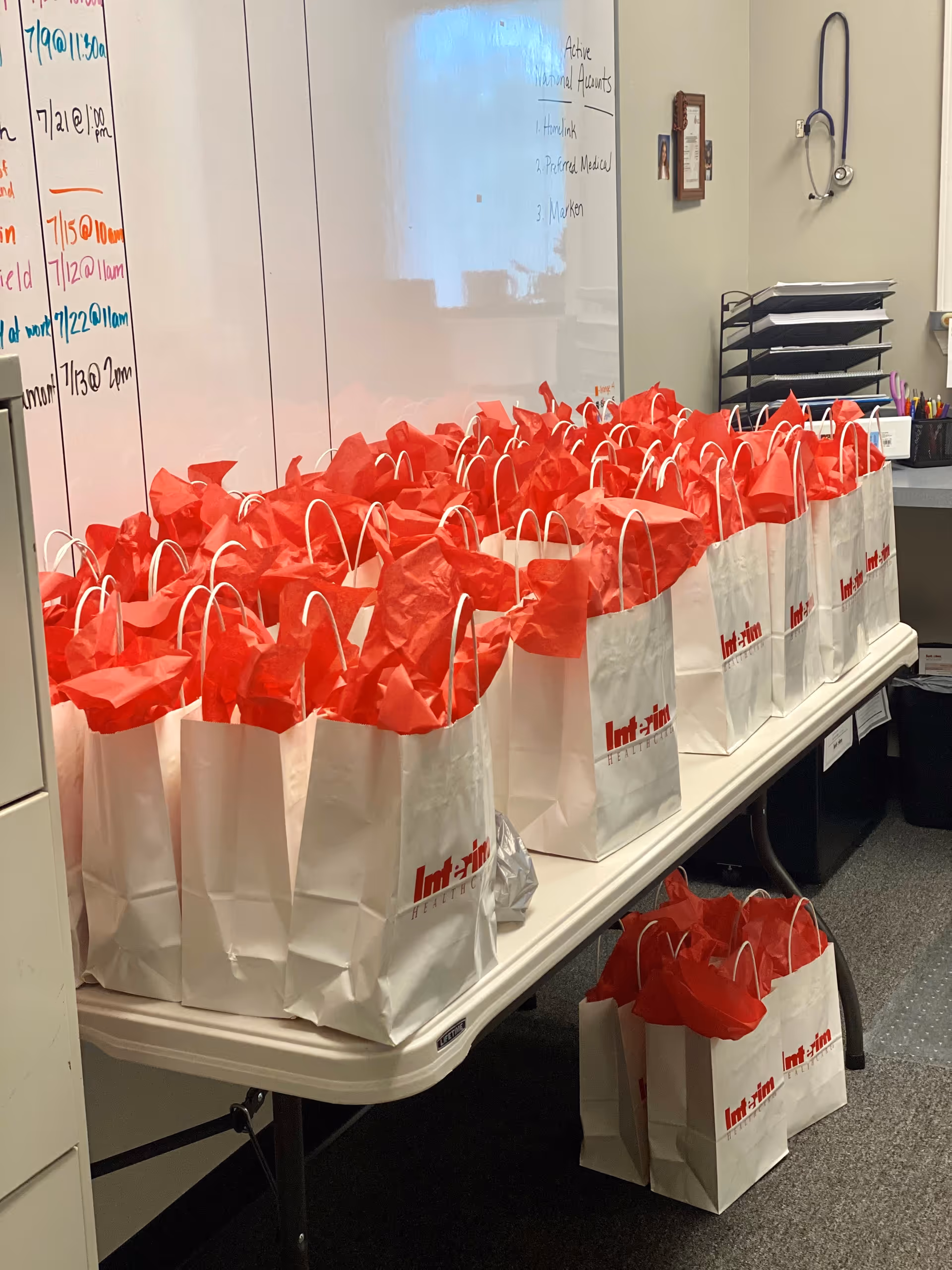Row of white gift bags with red tissue papers arranged on a table in an office.