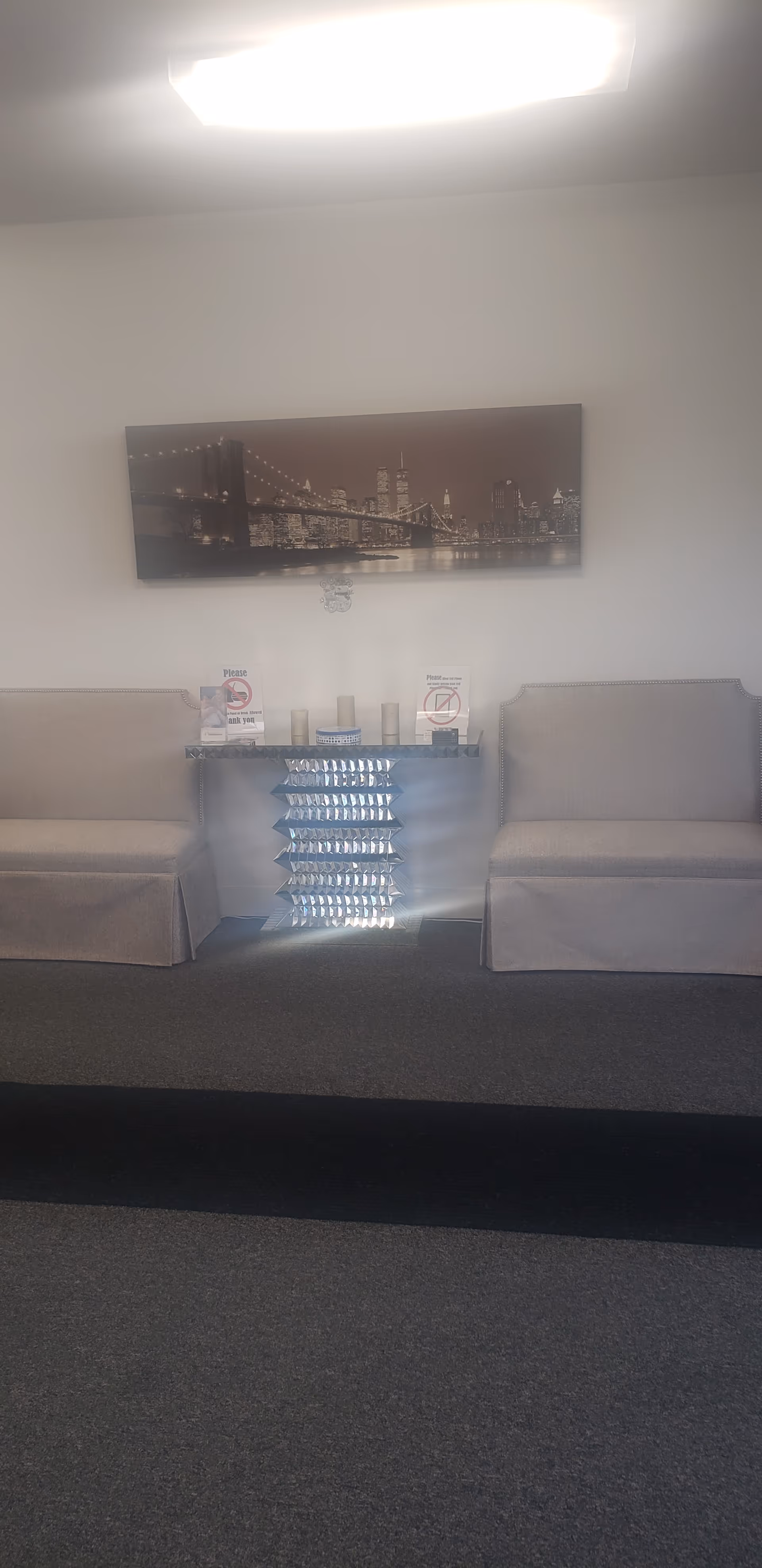 Two gray waiting-area chairs flank a display rack beneath cityscape wall art.