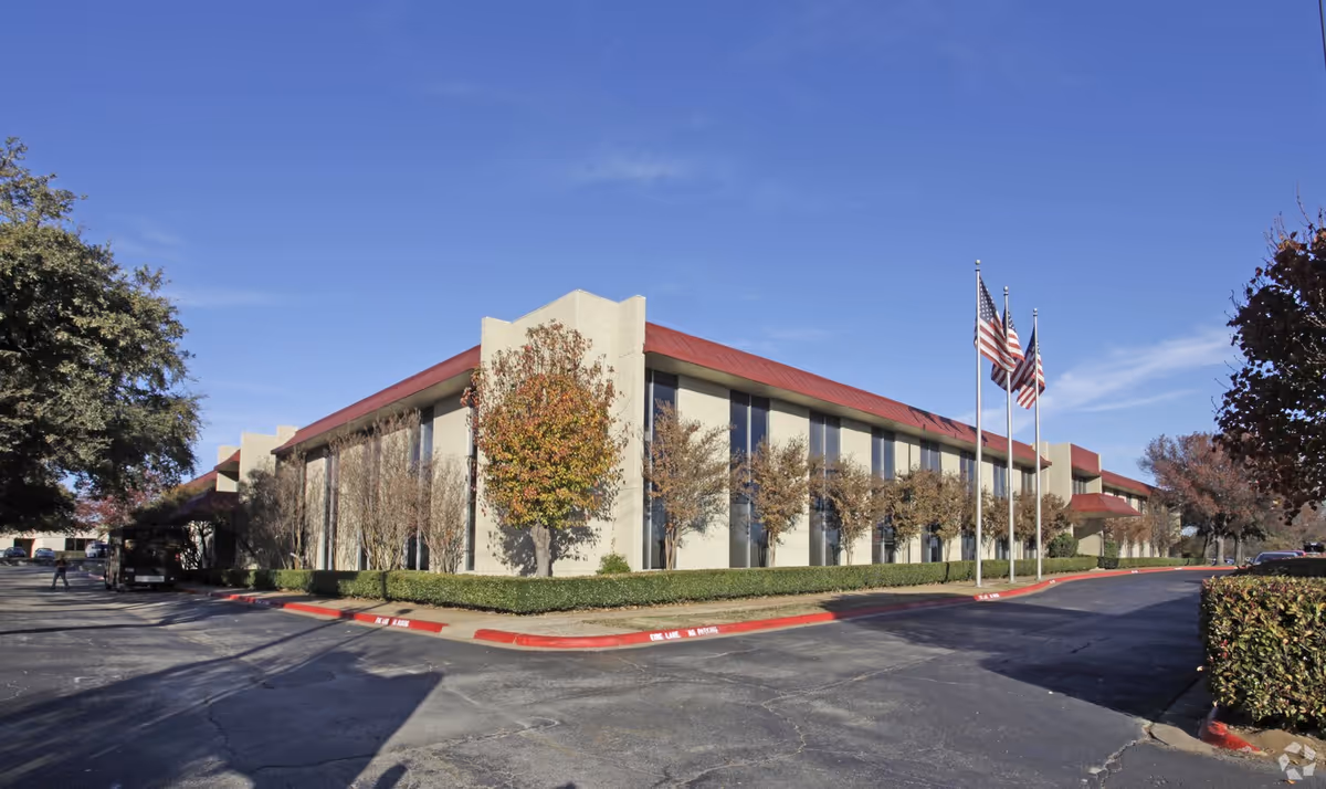 A single-story senior living facility with beige walls, red roof, and flagpoles in front.