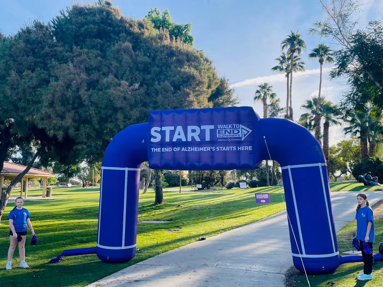 Blue inflatable START arch at outdoor park with volunteers and trees.