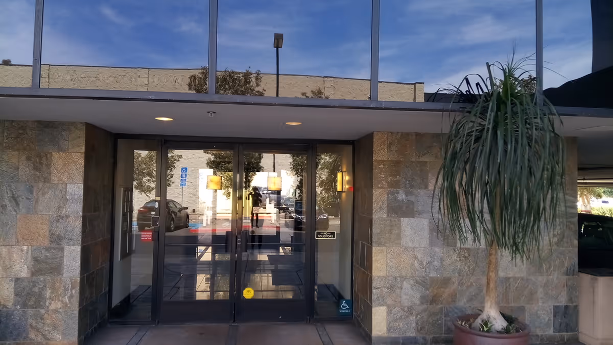 Stone-clad building entrance with glass doors and a tall potted plant outside.