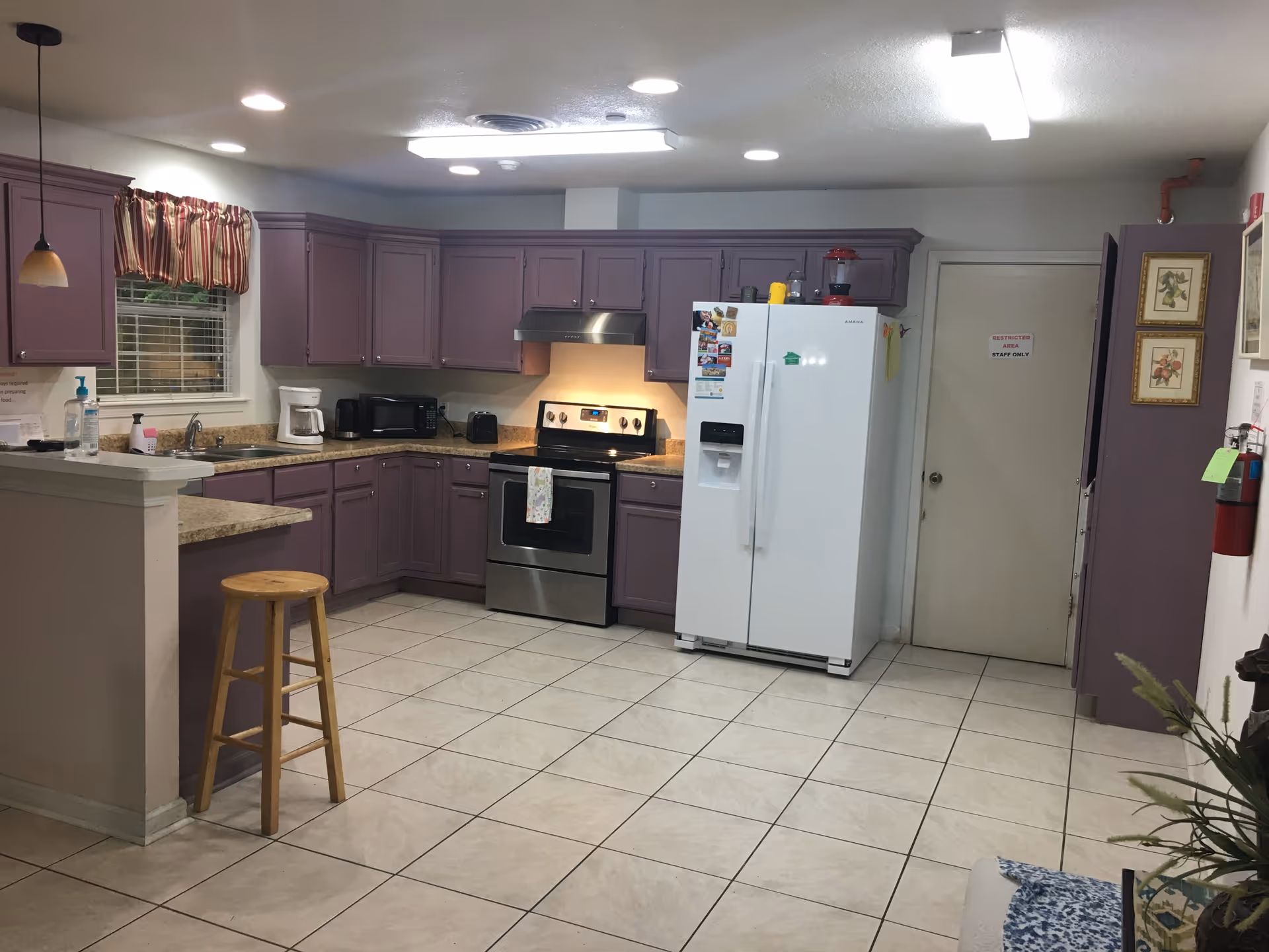 Spacious kitchen with purple cabinets, a stainless steel oven, white refrigerator, bar stool and tiled floor.