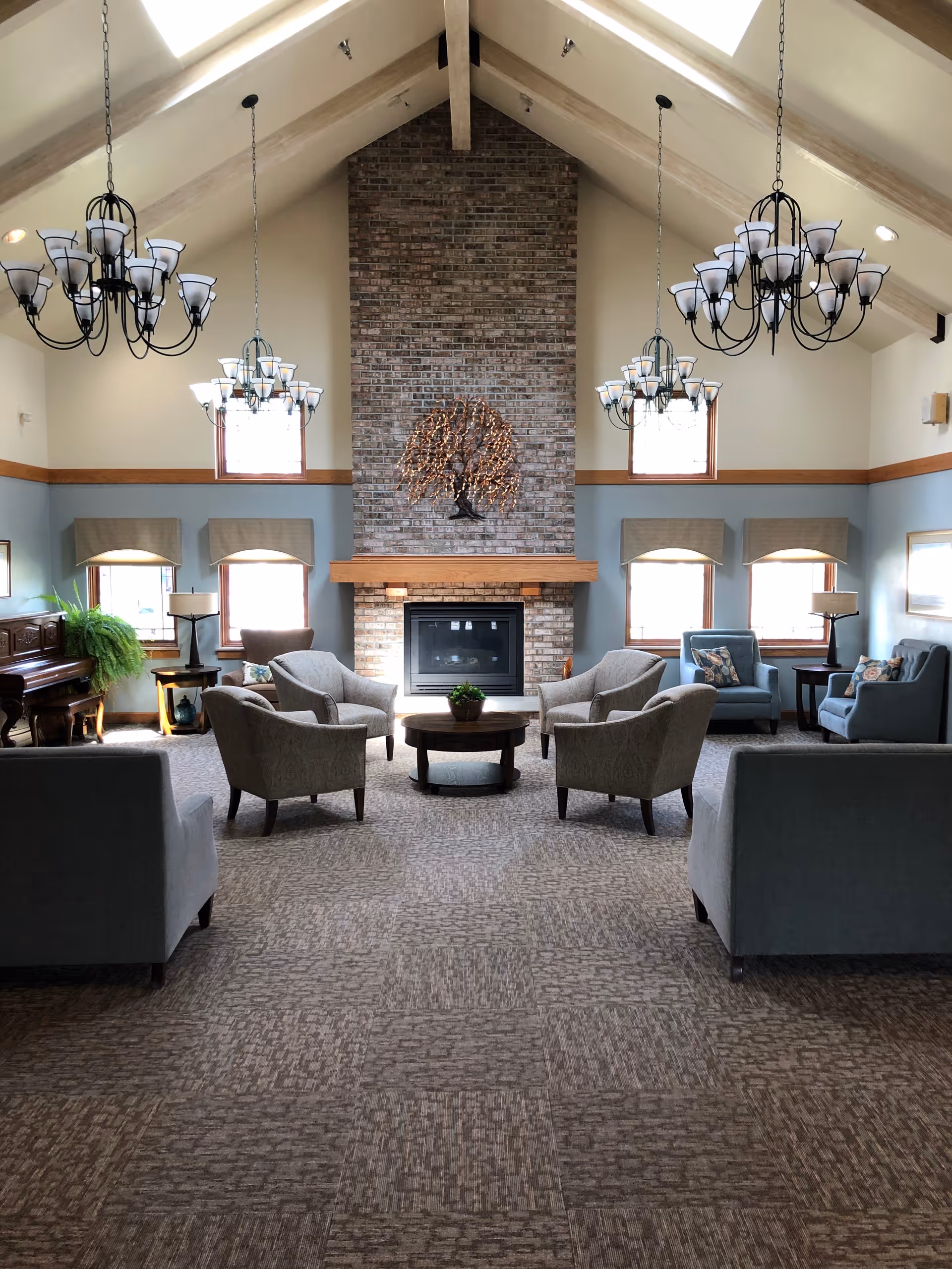 A spacious senior living lobby with a brick fireplace and circular seating around a coffee table.