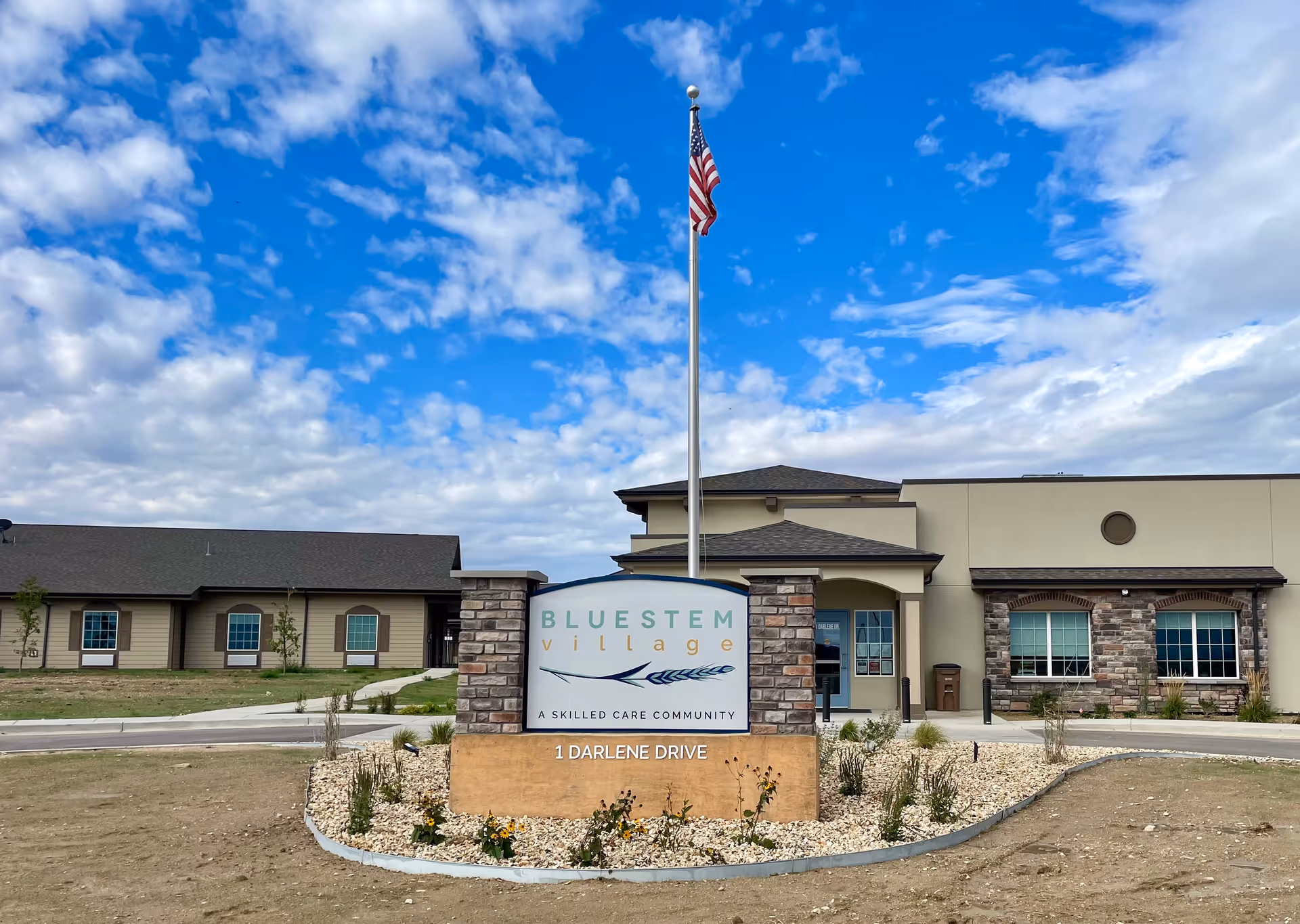 Bluestem Village exterior with flagpole and stone-front entrance sign