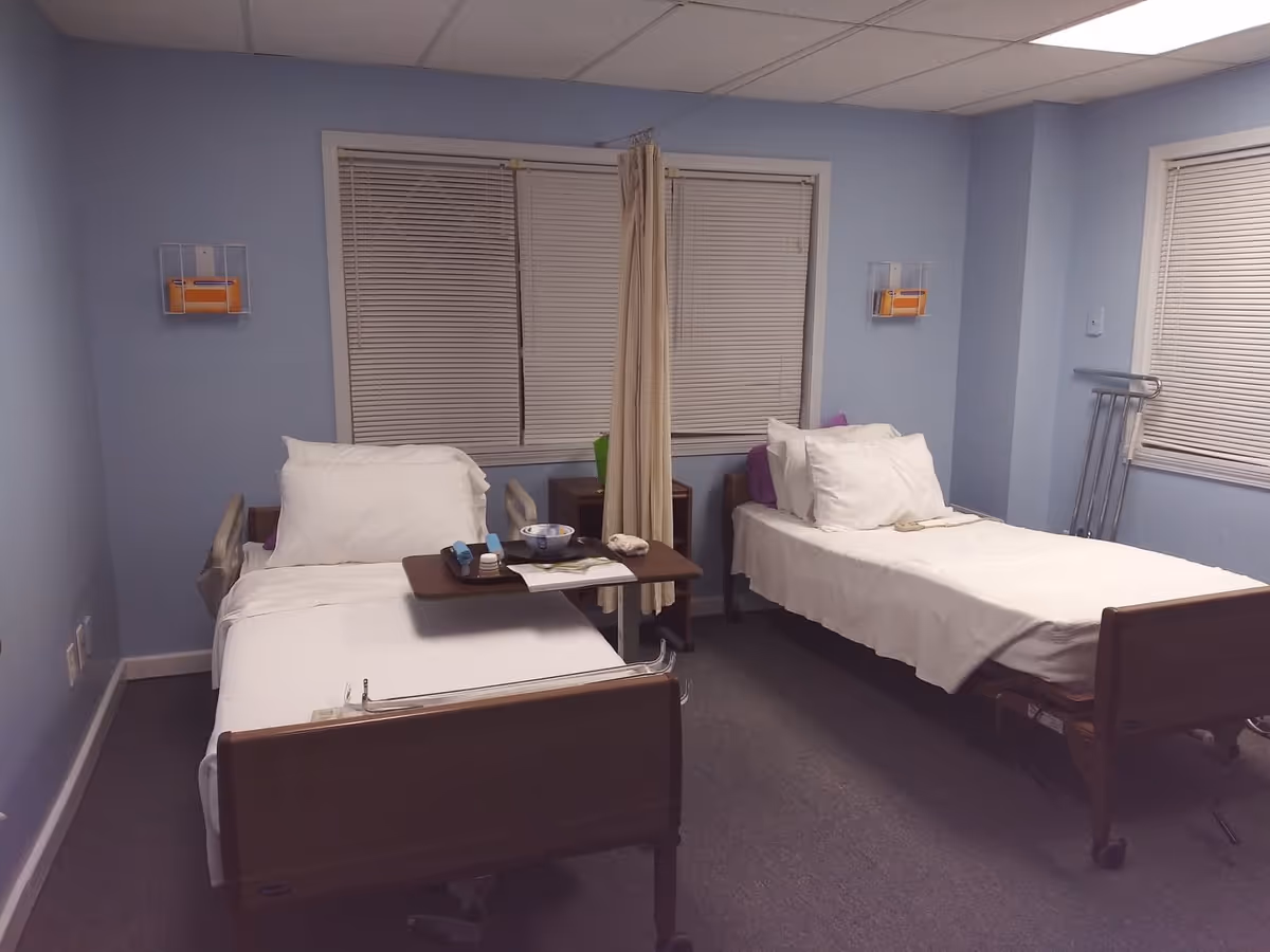 Two hospital-style beds with white linens and a shared overbed table in a blue room.