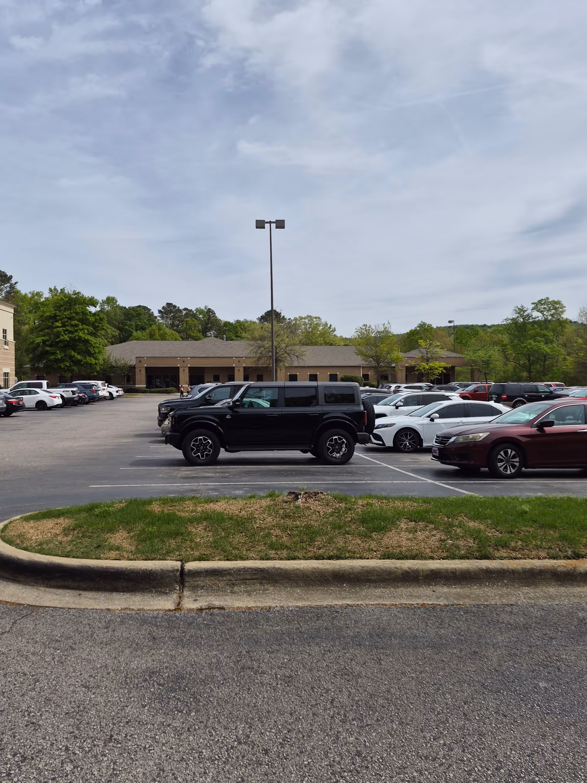 Parking lot in front of a beige, single-story building with many cars.