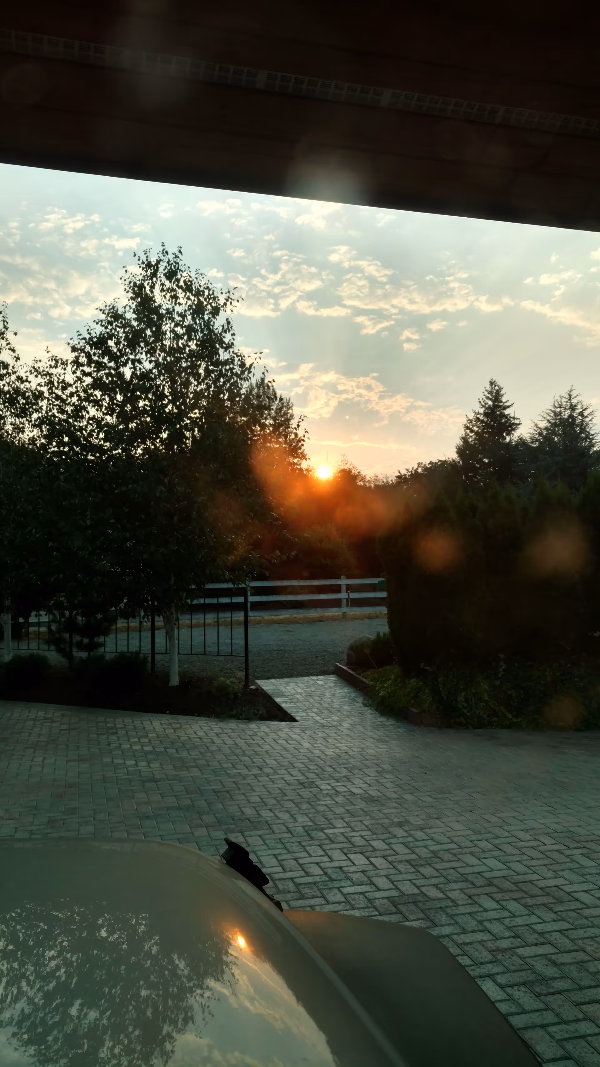 Sunset over a paved outdoor courtyard with trees and a fence.