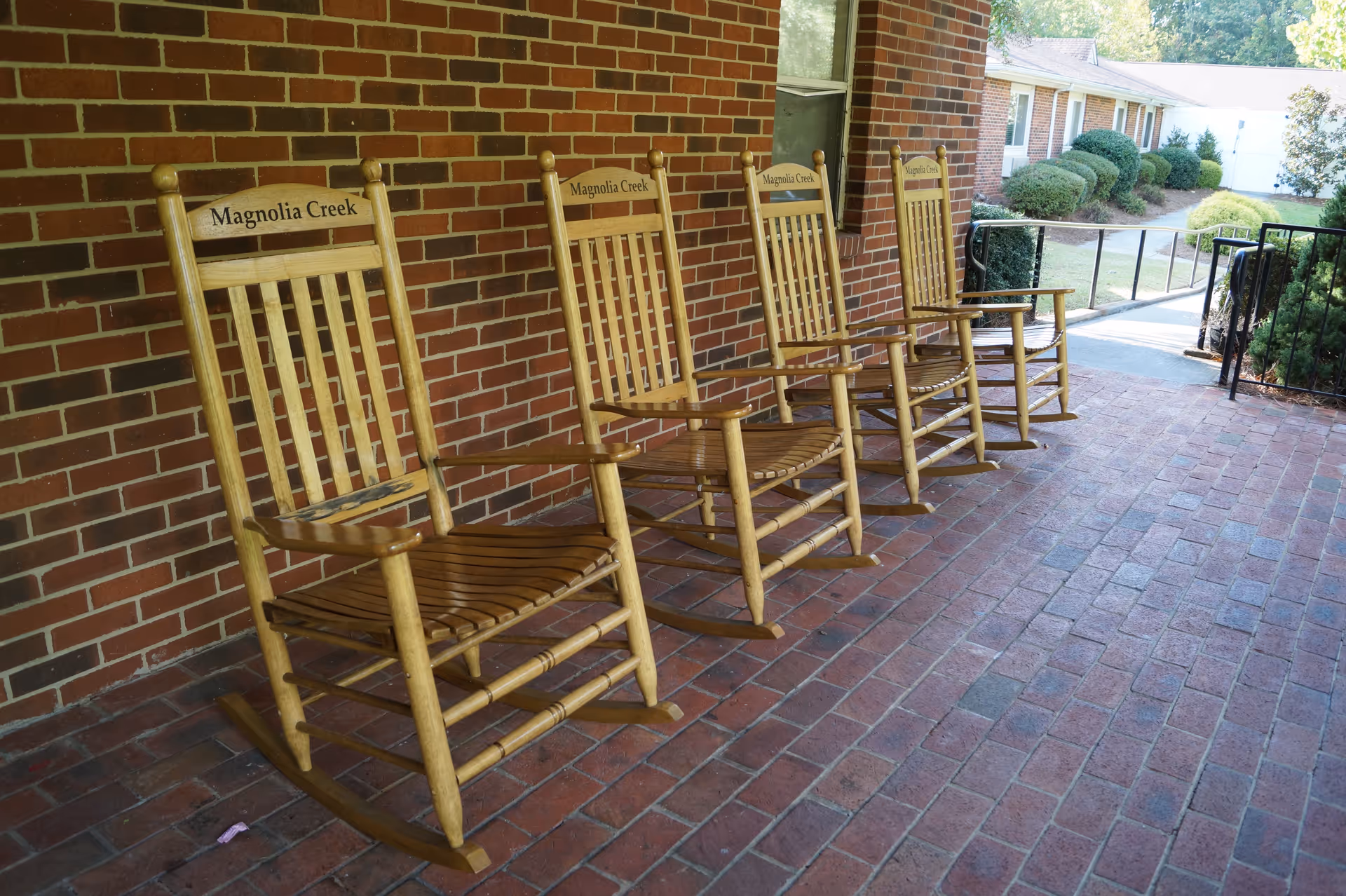 Four wooden rocking chairs labeled "Magnolia Creek" lined up on a brick front porch.