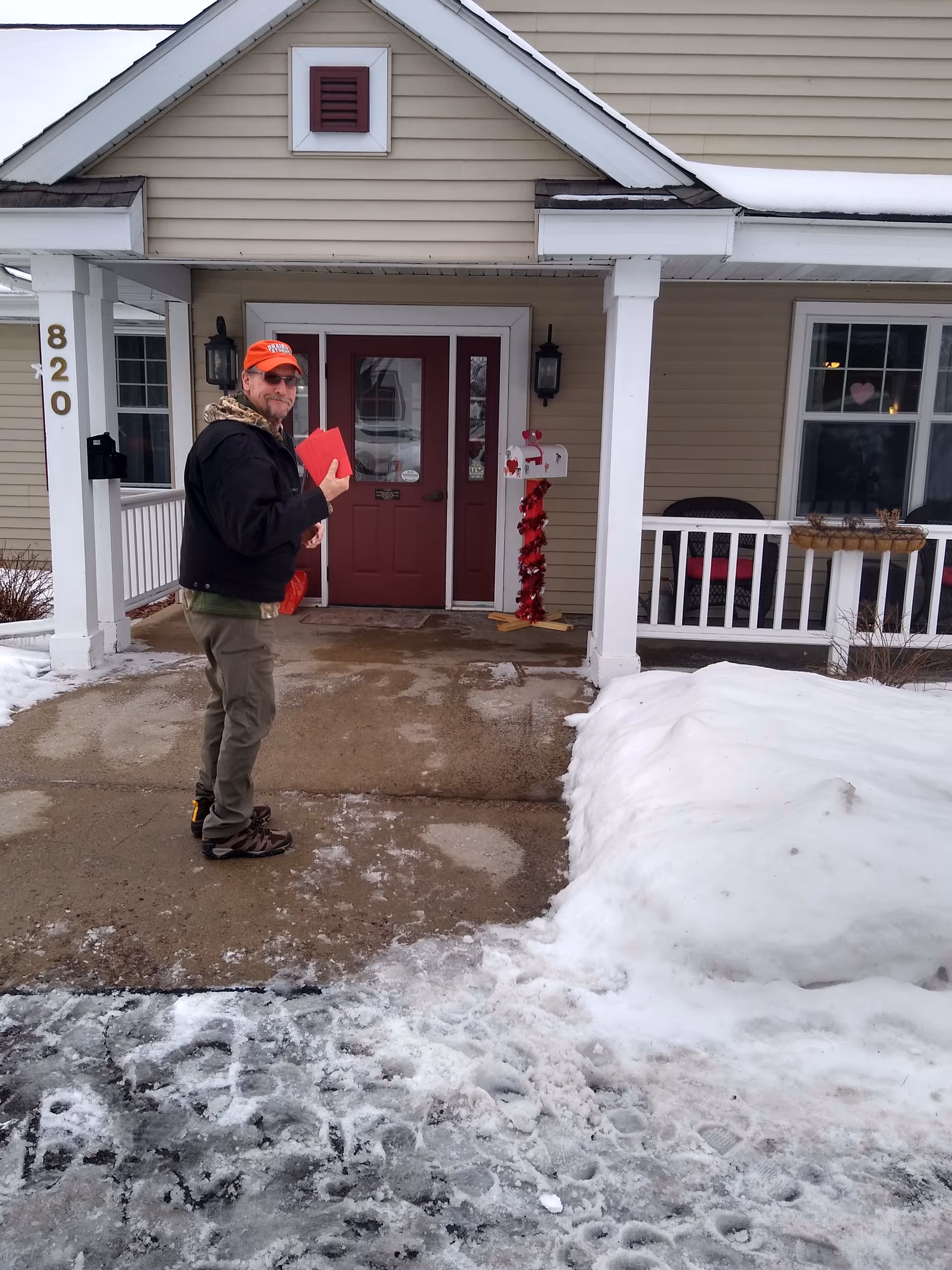 Man stands on a snowy walkway outside the red front door of memory care facility.