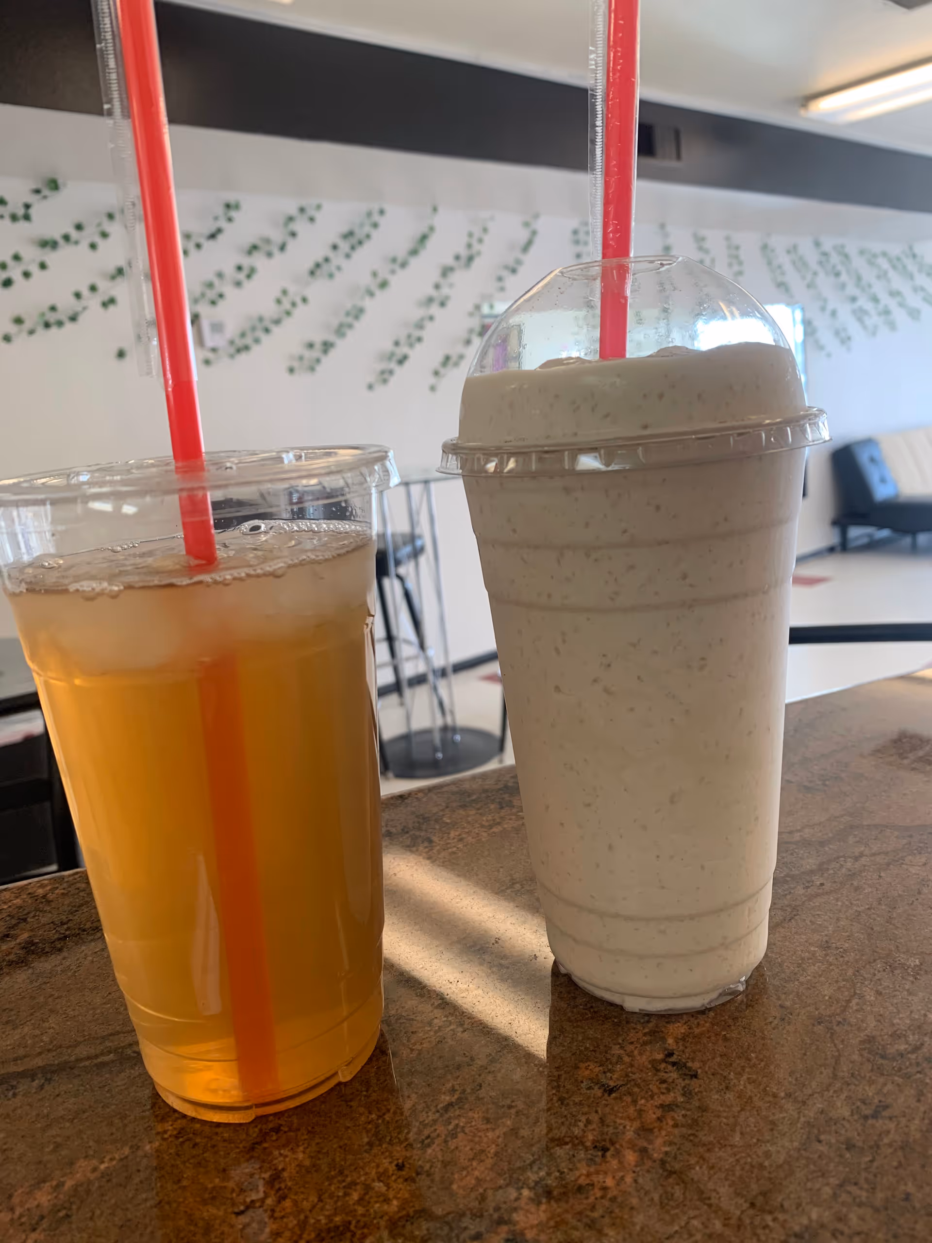 Two beverage cups with red straws sit on a marble counter inside a lounge area.