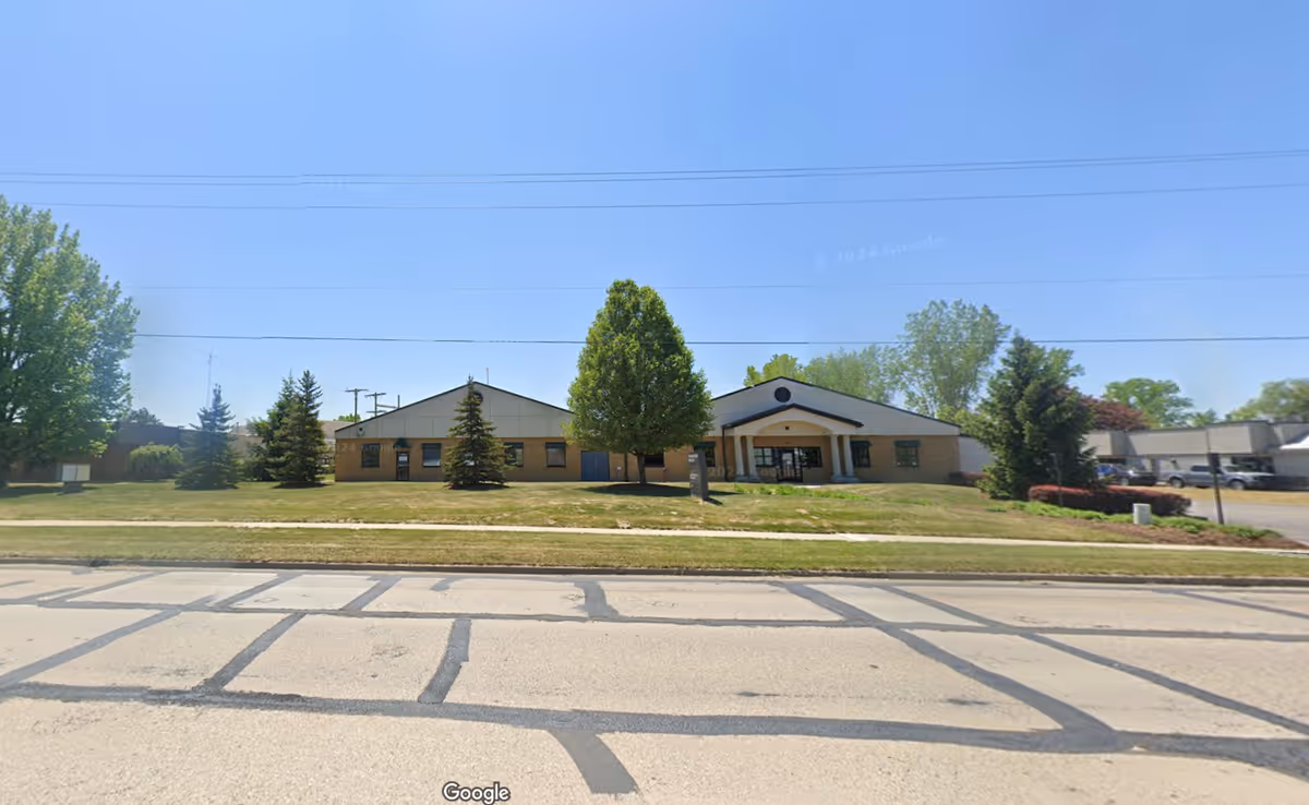 Exterior view of a single-story medical facility with a lawn, trees, and a driveway.