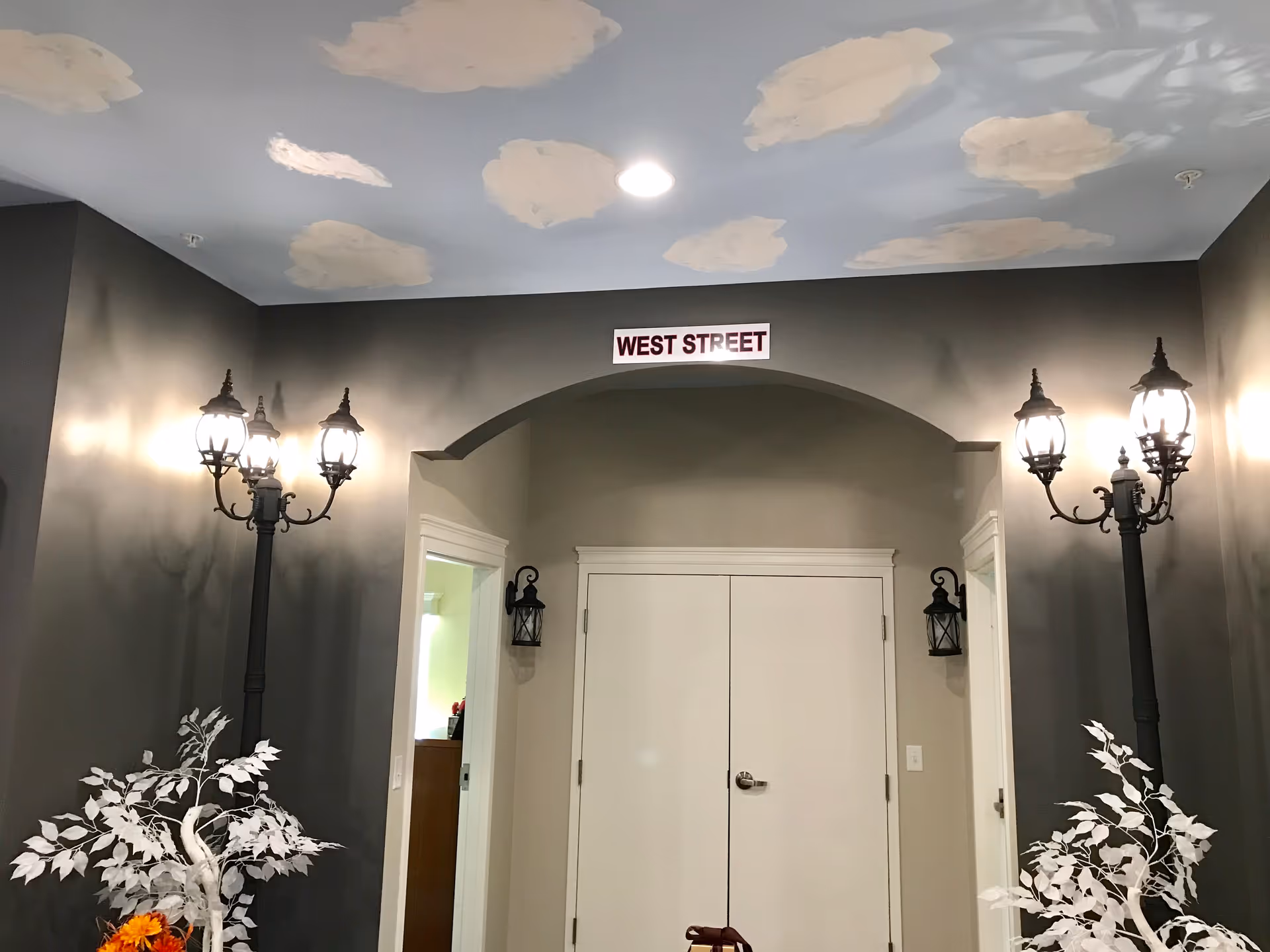 Interior hallway with archway, cloud-painted ceiling, decorative lamps, and a West Street sign.