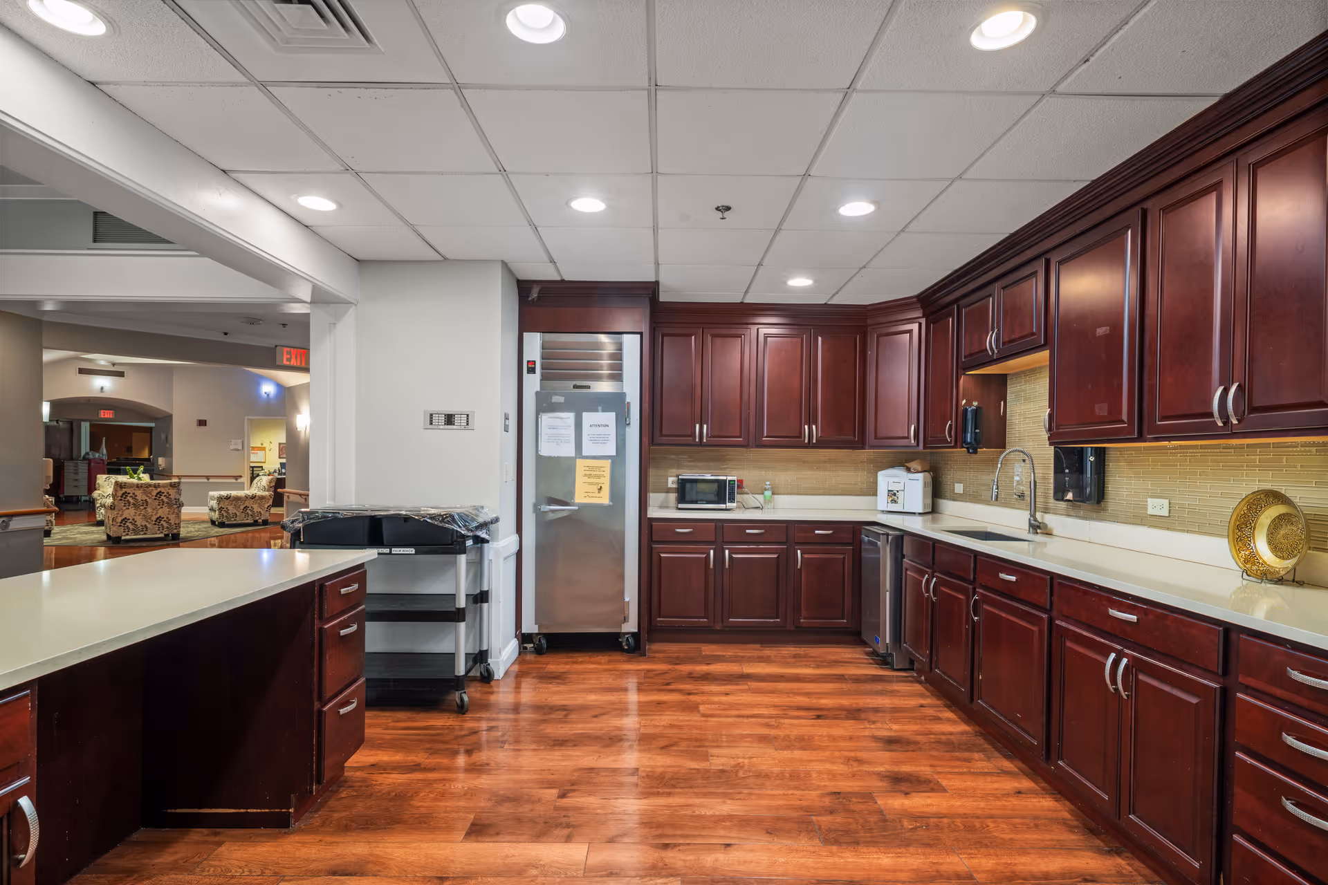 Communal kitchen with dark wood cabinets, white countertops, and stainless appliances in a senior living facility.
