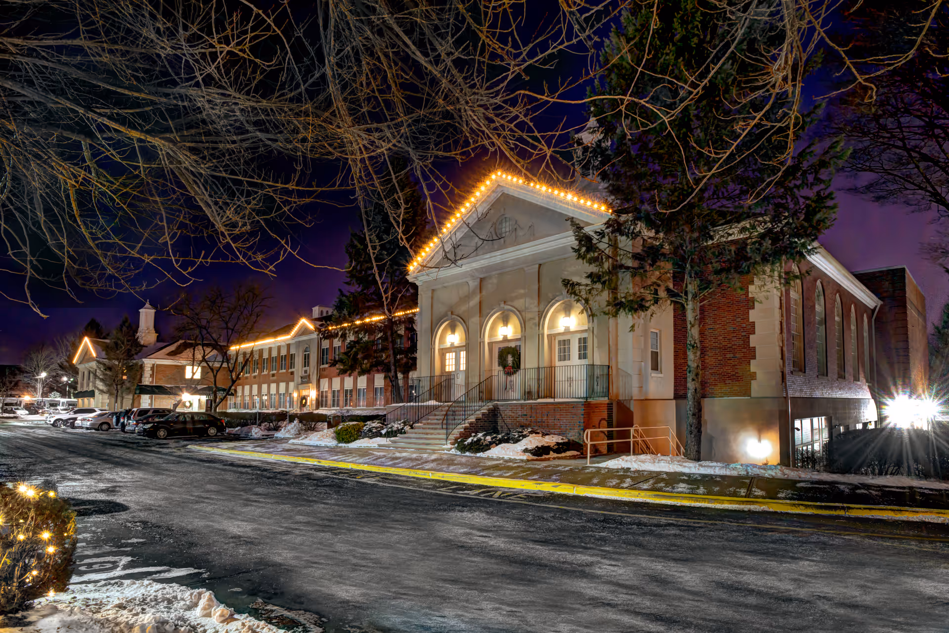 Night exterior view of Siena Village at Wayne with lit entrance and snowy street.