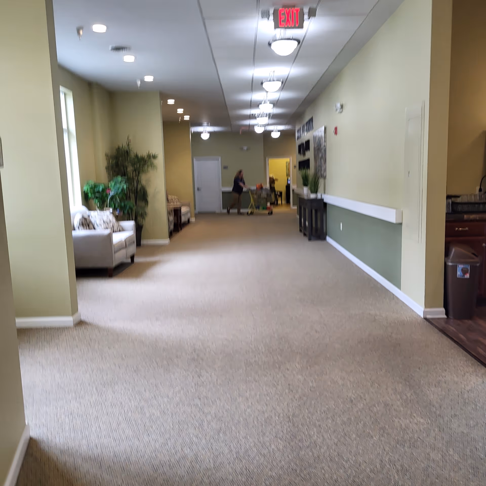 Long hallway in a senior living facility with seating, decor, and distant staff.