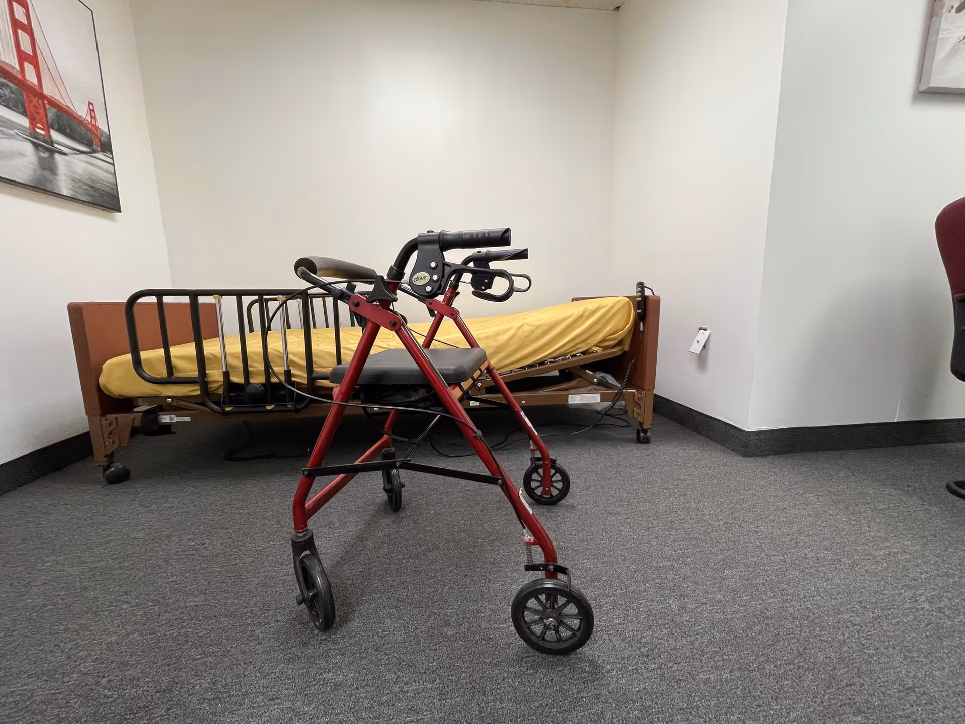 Interior patient room with a hospital bed and a red walker in front.