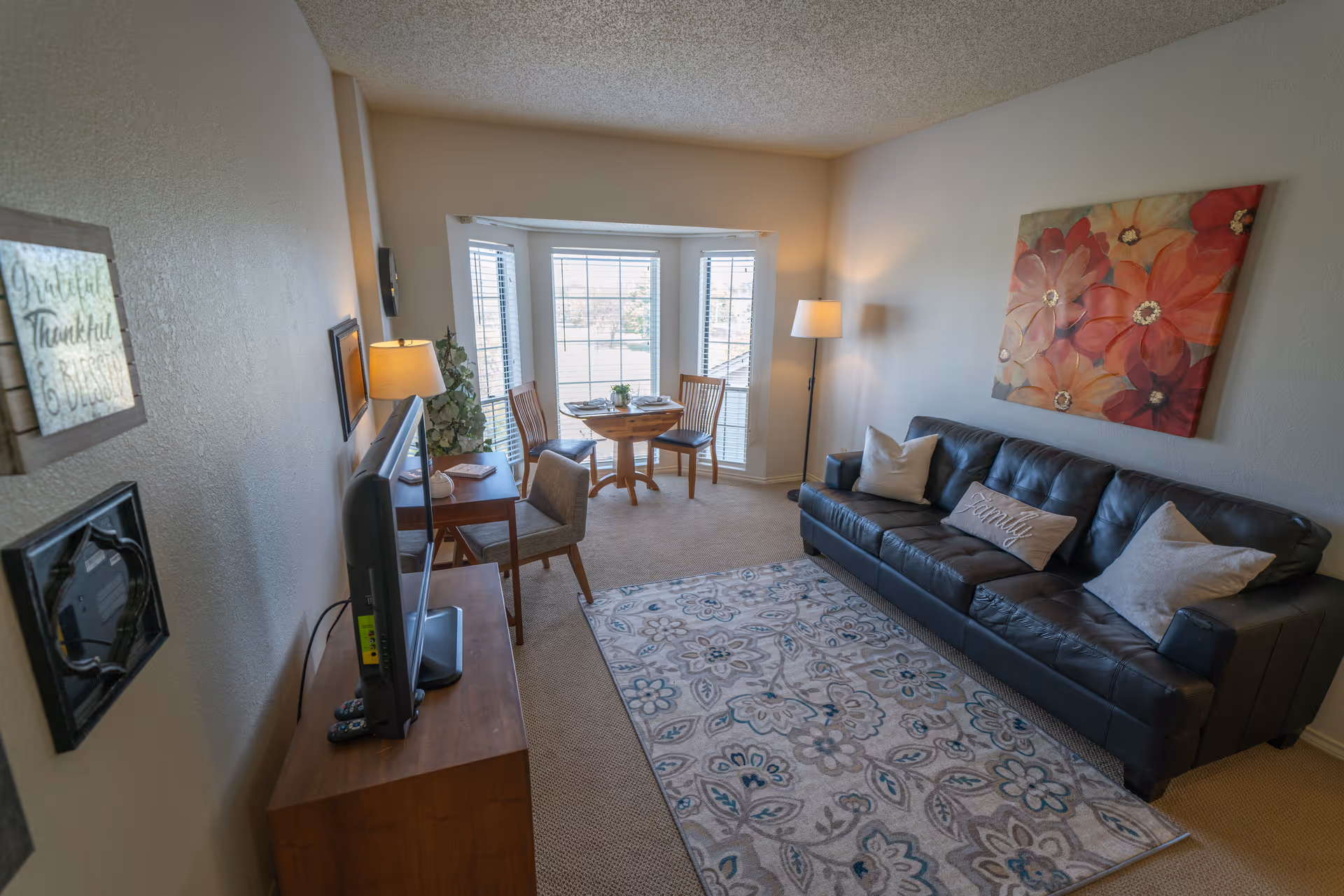 Cozy living room with leather sofa, rug, art, and bay-window seating.