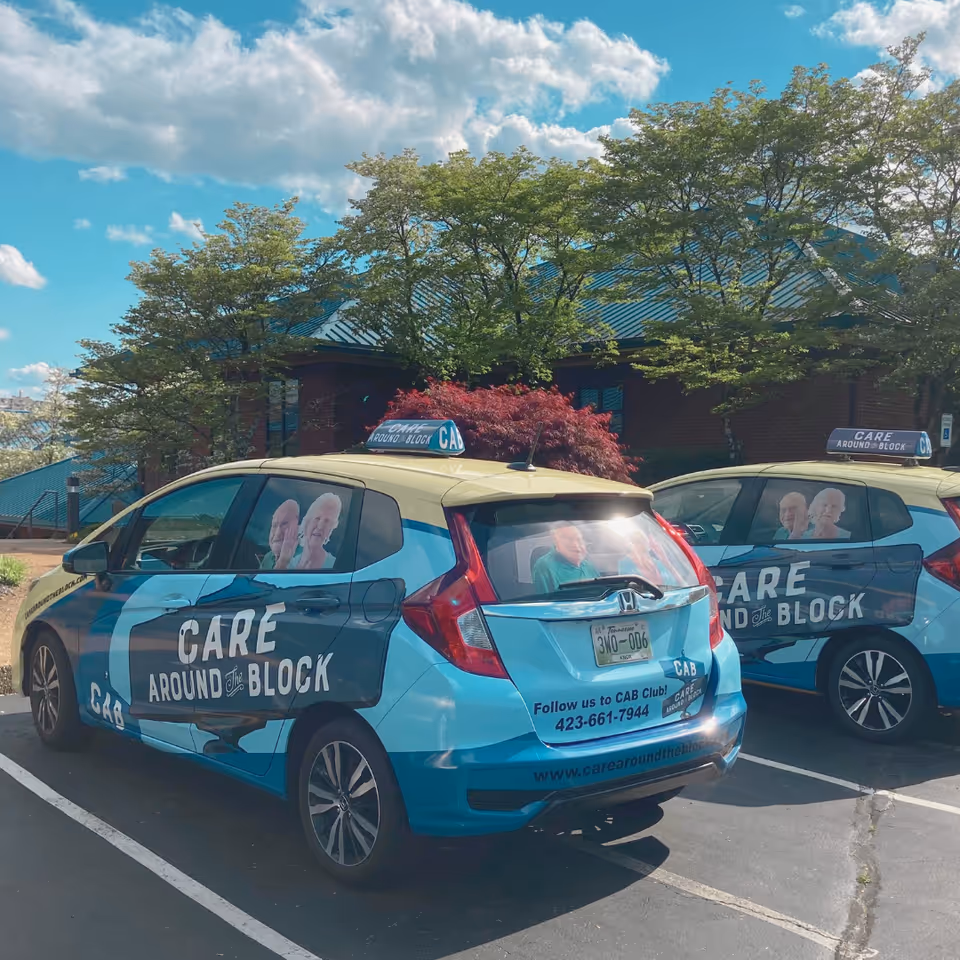 Blue Care Around the Block branded vans parked in a lot beside a brick building.