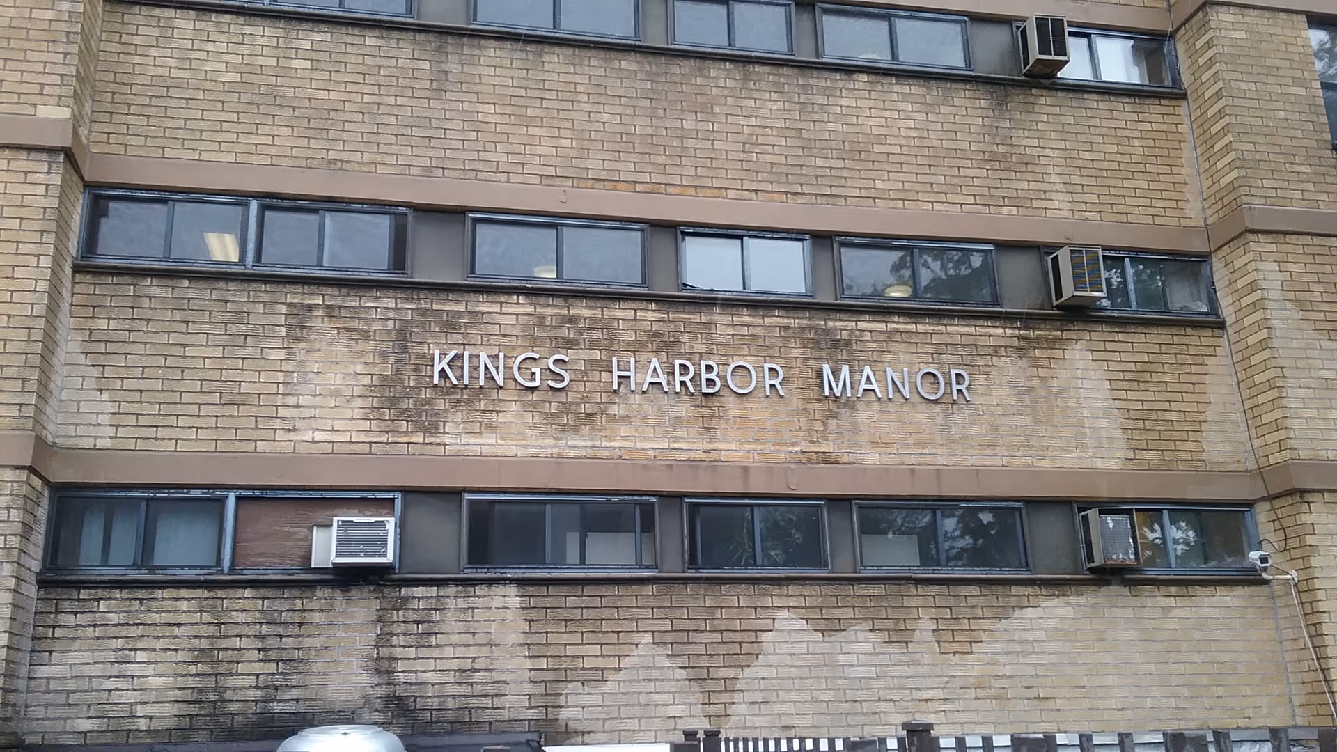 Brick building exterior with Kings Harbor Manor sign on the front facade and rows of windows.