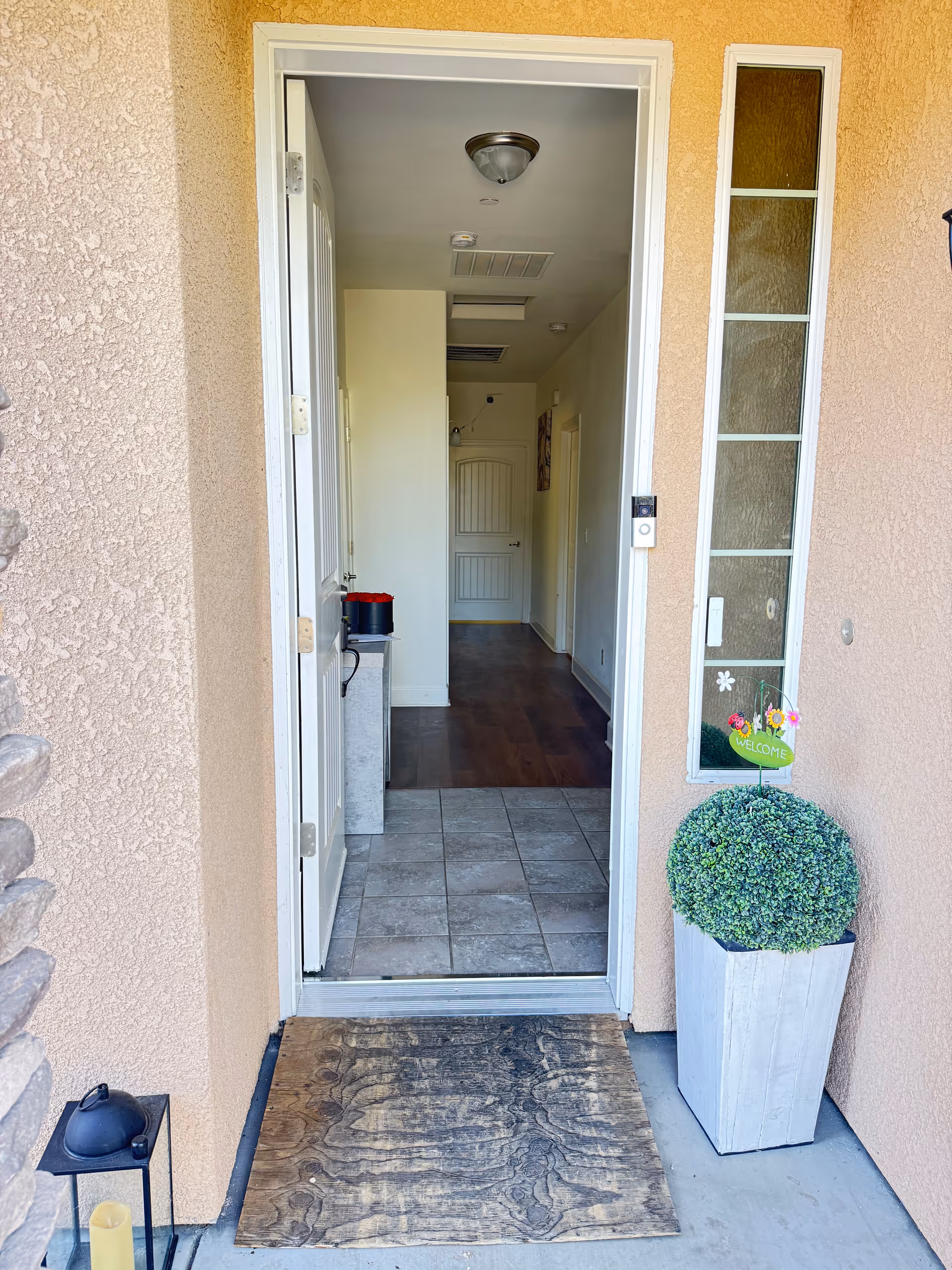 Open doorway leads into a hallway with tiled entry, interior doors, and a welcome plant outside.