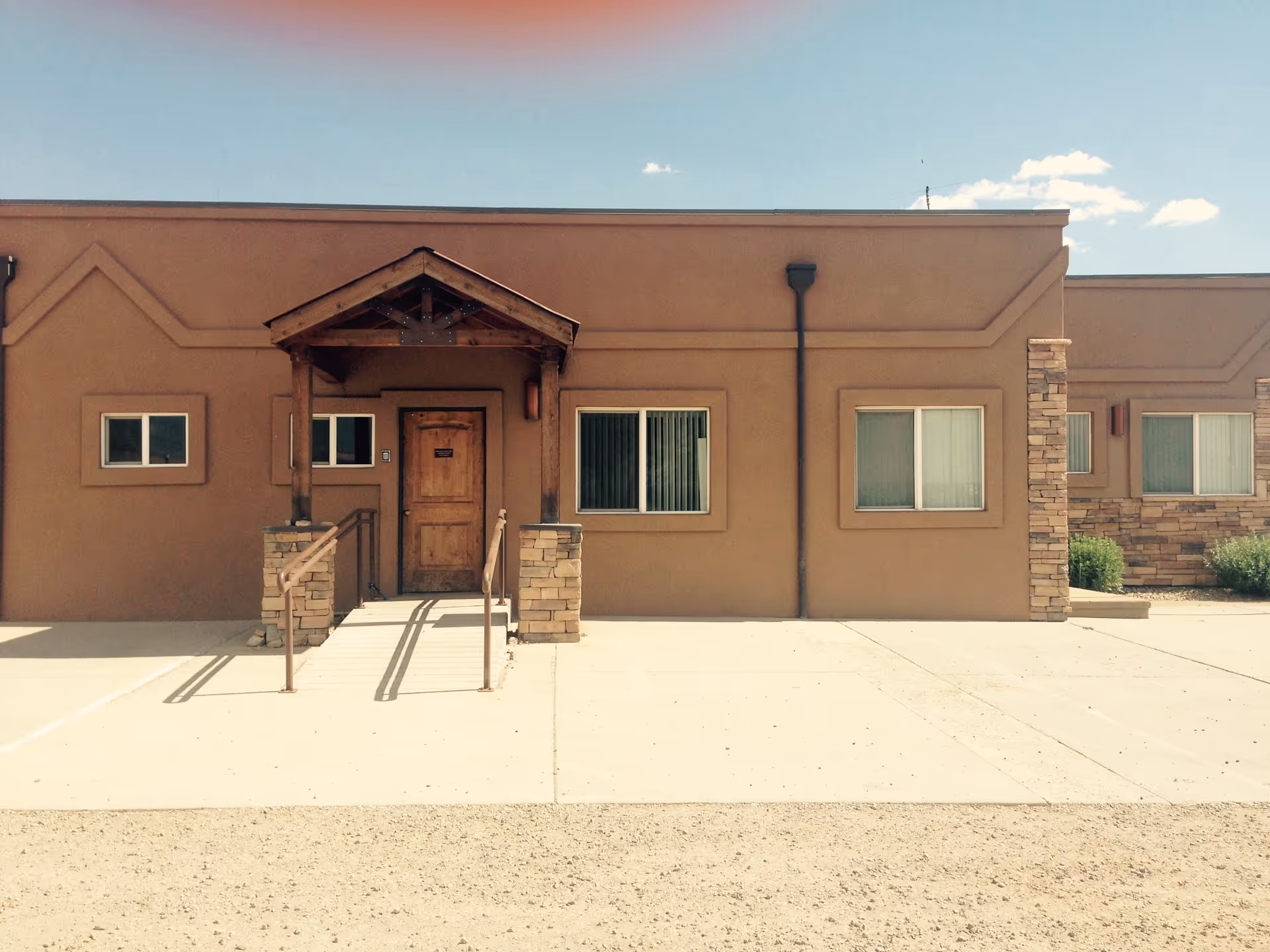 Exterior of a single-story tan hospice building with front entrance and ramp.