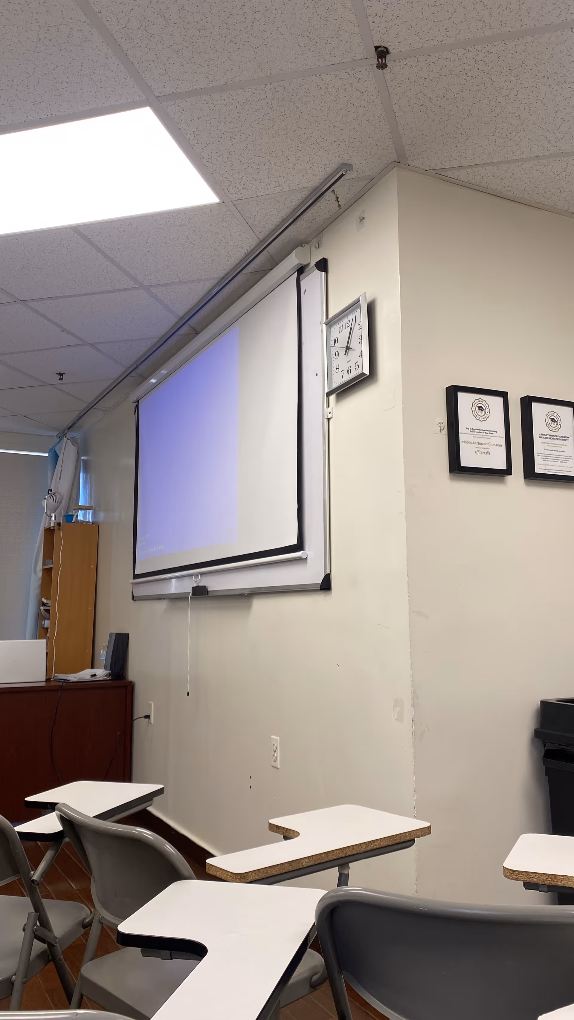 An interior training room with a projector screen, clock, certificates, and student desks.