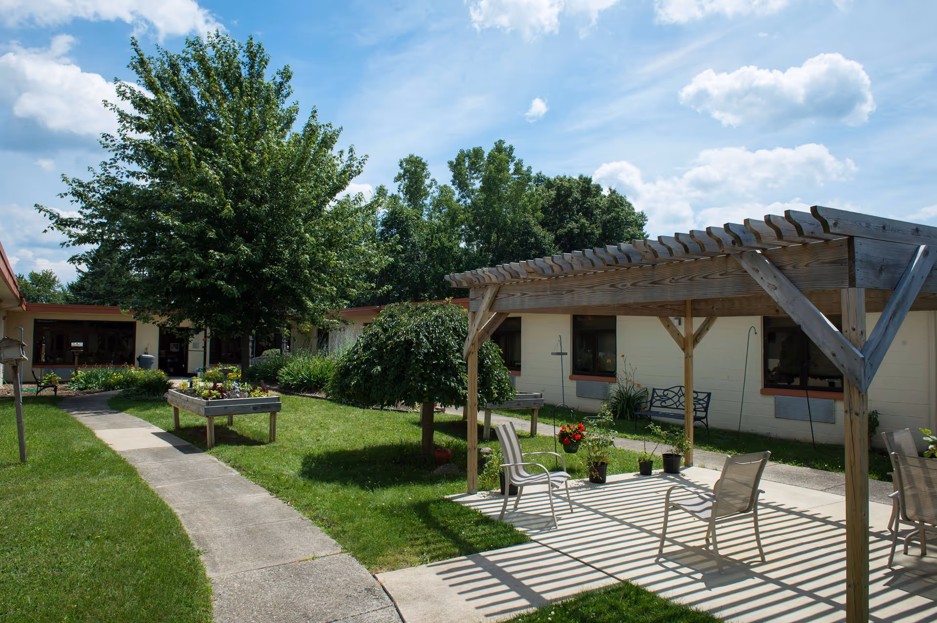 Outdoor courtyard of Howell Care Center with a wooden pergola, chairs, and greenery.