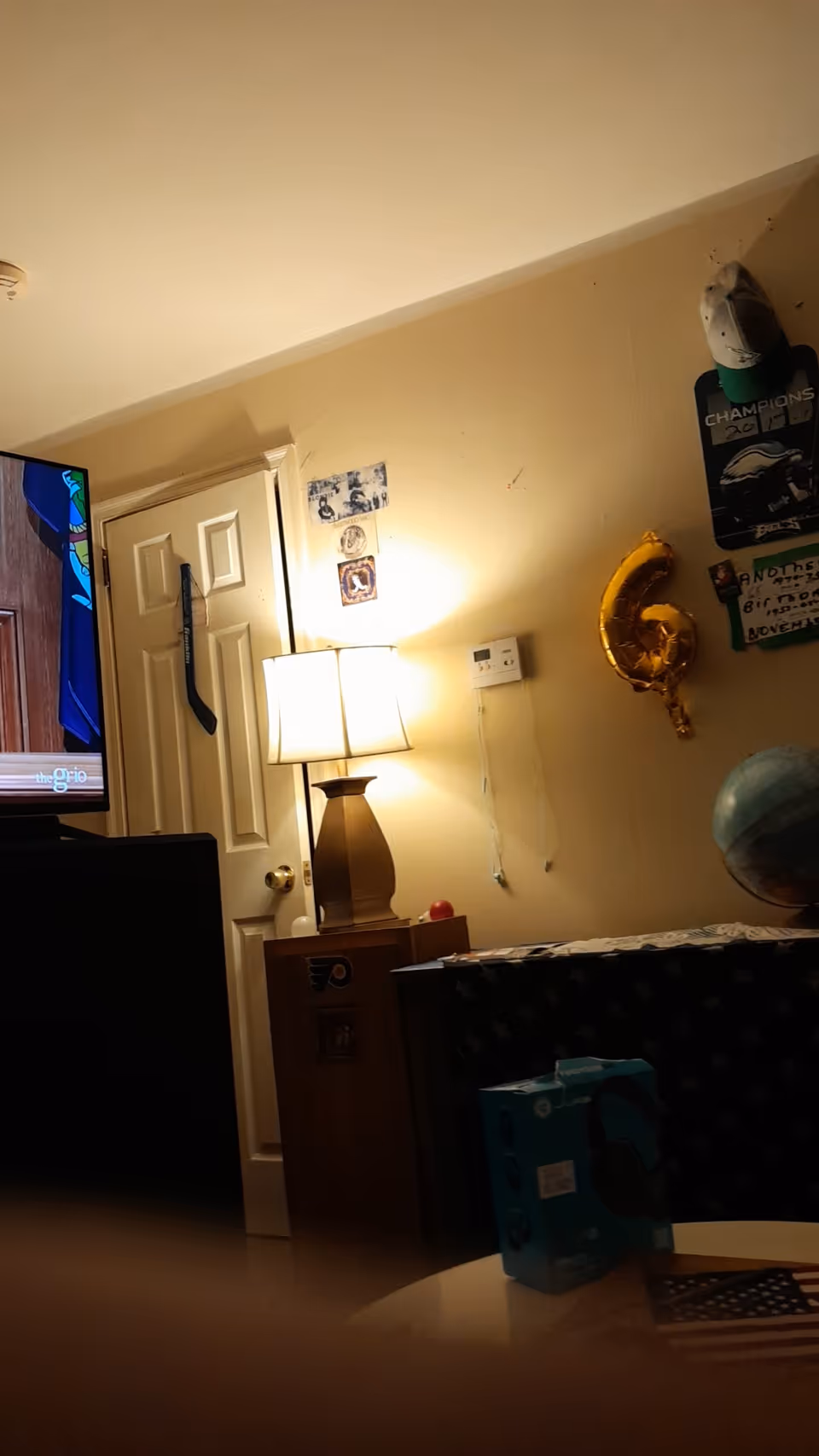 Cozy living room with TV, lamp, door, wall decor, a globe, yellow 6 balloon, and table.