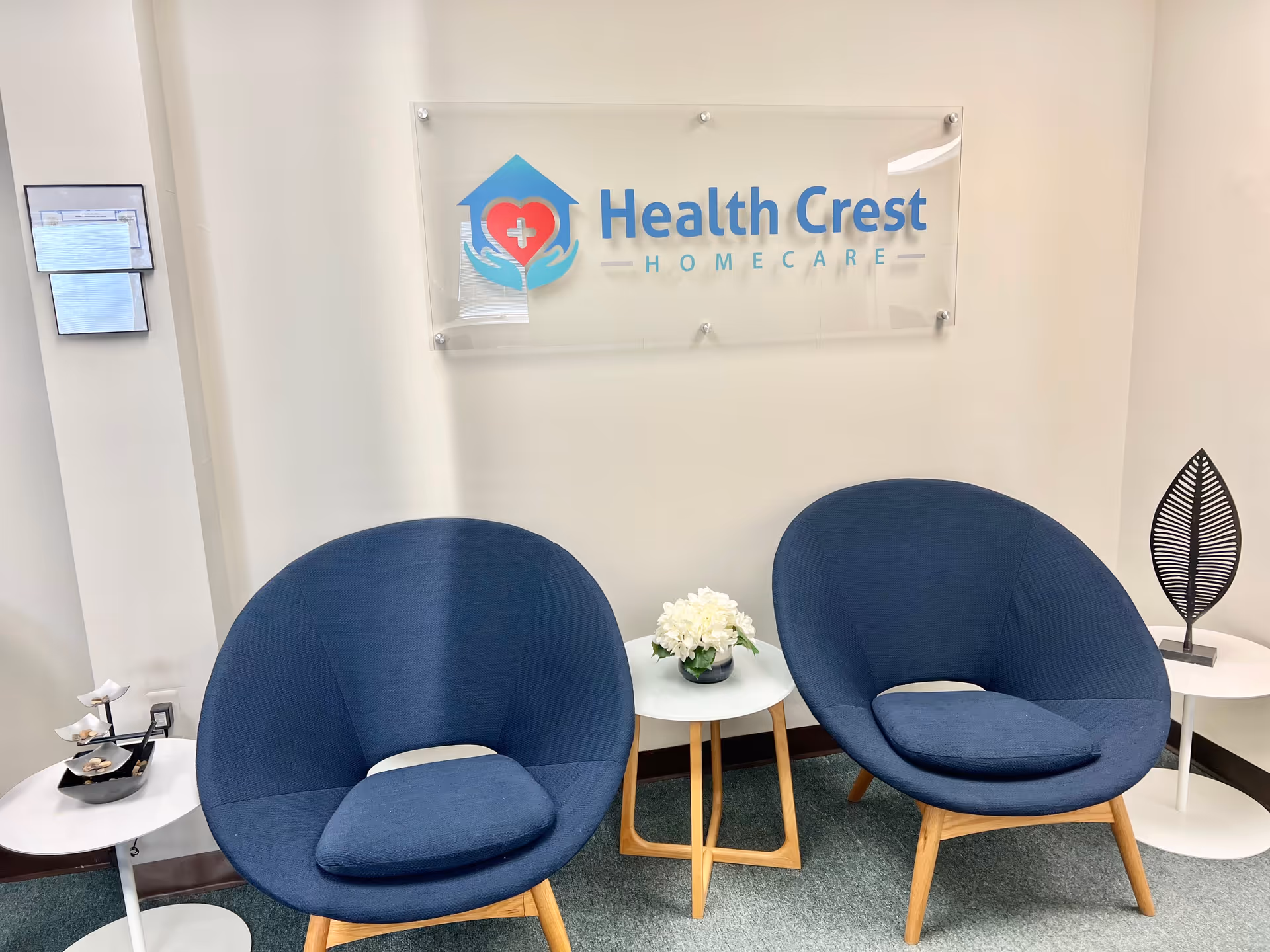 Lobby seating area with two blue chairs, small tables, and a Health Crest Homecare sign.