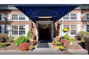 Exterior view of a senior living facility entrance with a blue canopy and potted plants.
