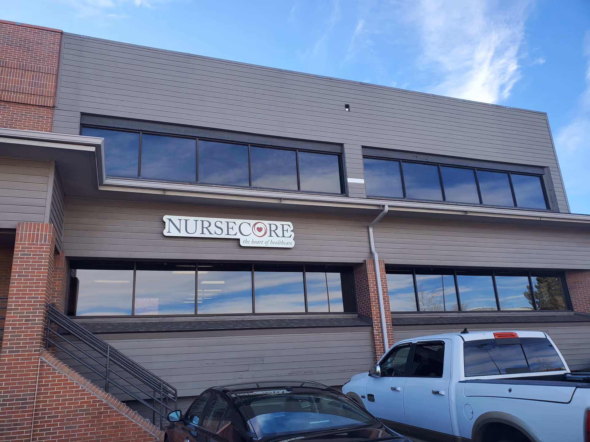 Exterior view of a NurseCore building with large windows and parked vehicles in front.