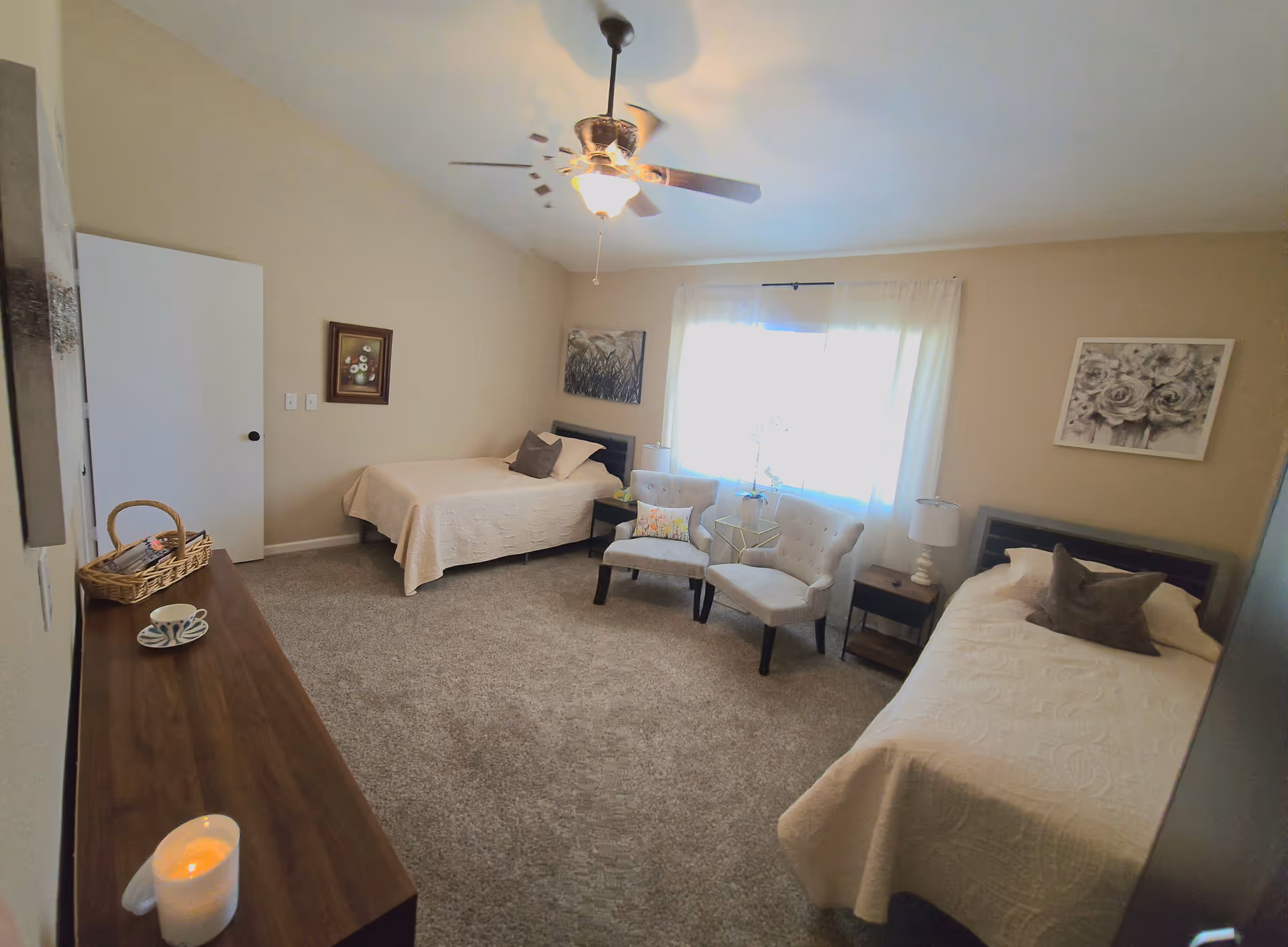 Two beds in a beige senior living bedroom with seating area by a window.