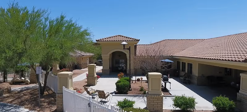 Outdoor courtyard of memory care facility with benches, a covered entry, and sunny skies.
