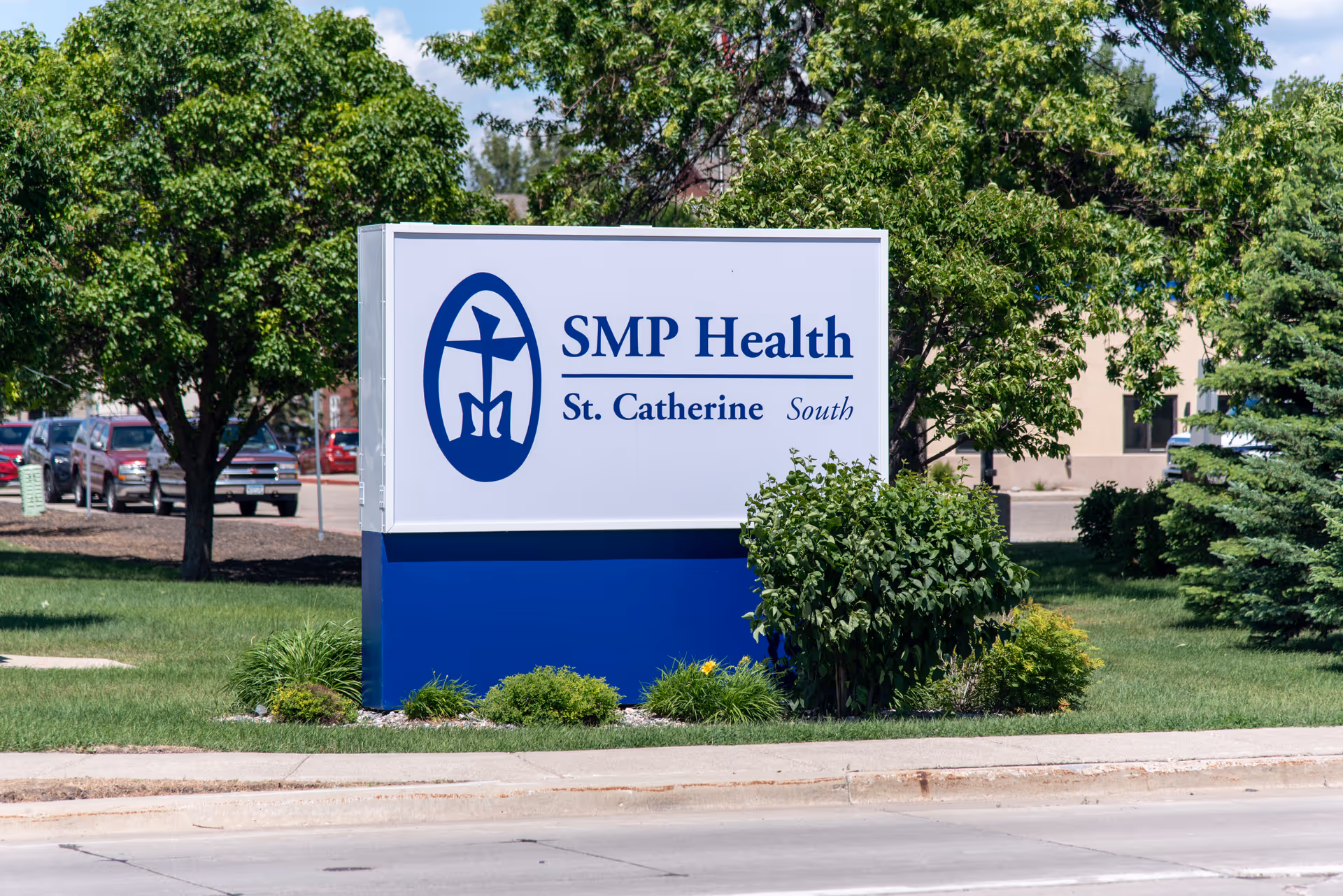 Outdoor sign reading "SMP Health St. Catherine South" placed on a lawn with trees and a building in the background.