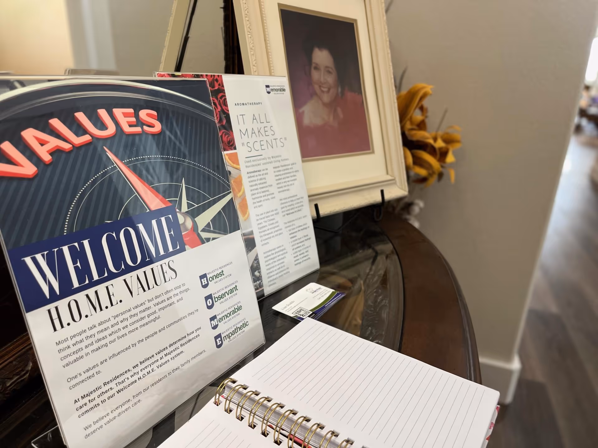 Brochures and a framed photo on a curved glass table in a senior living lobby.