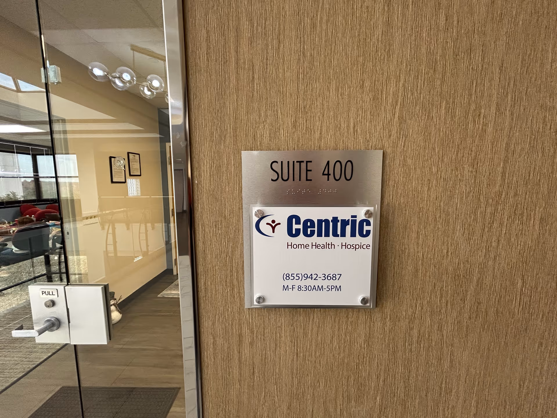 Wood-paneled wall with Centric Home Health sign beside glass entrance door, Suite 400.